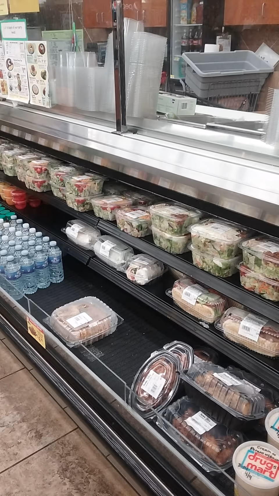 Inside a Discount Drug Mart refrigerated deli case with salads, desserts, and bottled water.