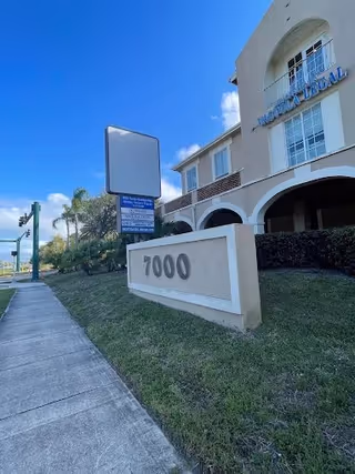Exterior view of a care facility building with arches and a 7000 sign under blue sky.