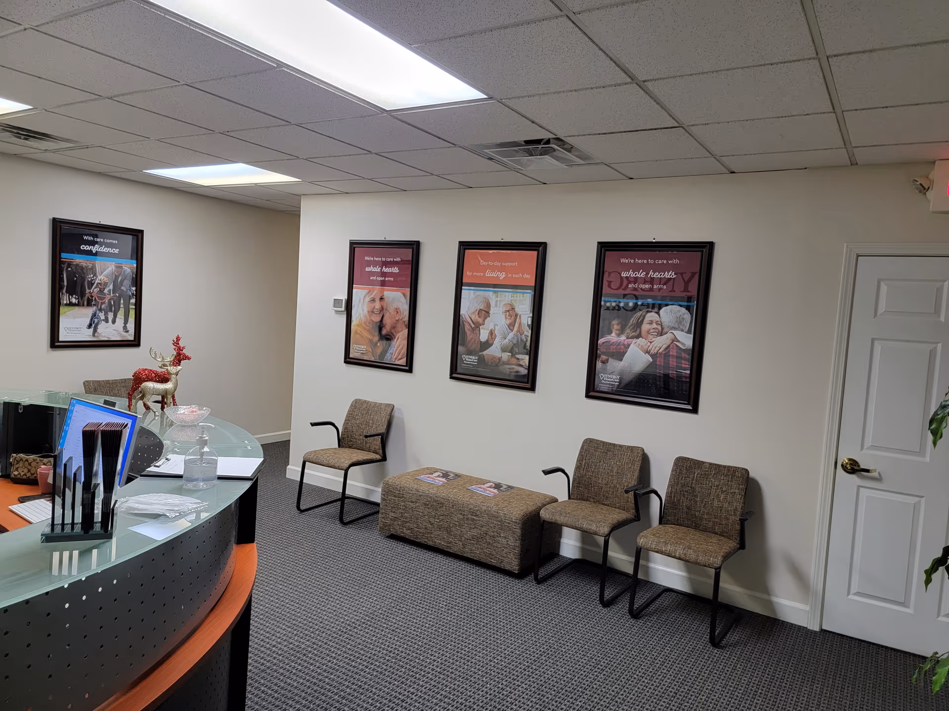 Interior reception area with a curved glass desk, framed posters, and waiting chairs.