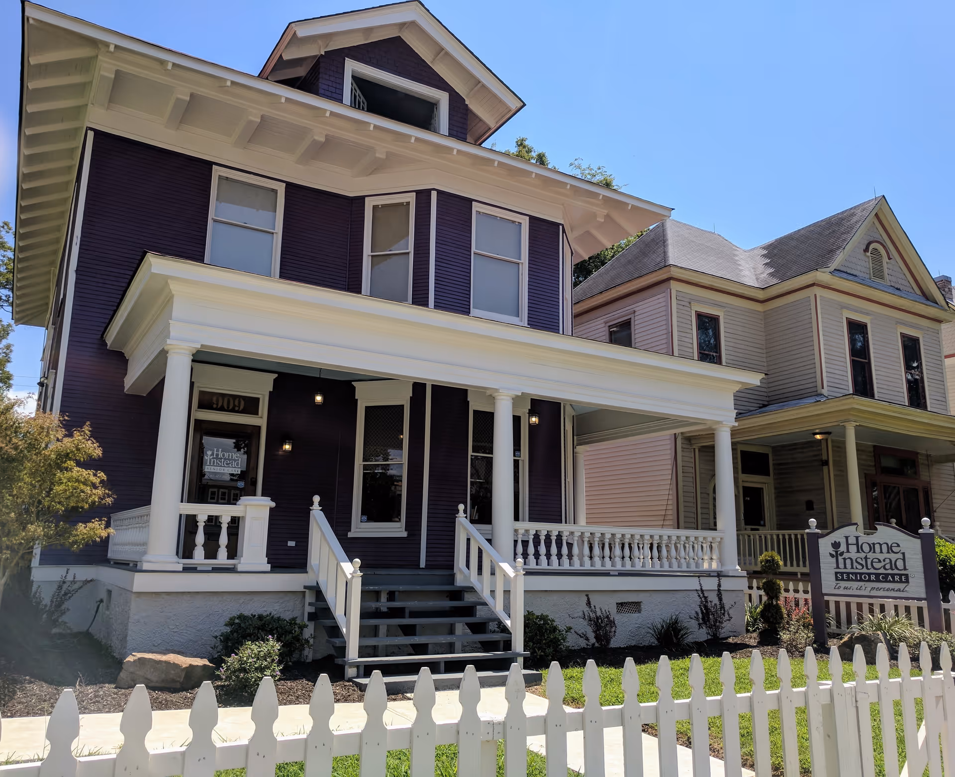 Two-story purple house with a wide front porch and Home Instead Senior Care sign.
