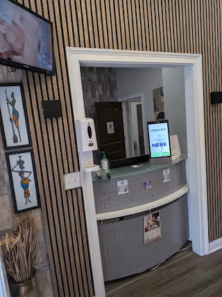 Reception desk with curved counter, striped walls, sanitizer, and a digital sign in a lobby.