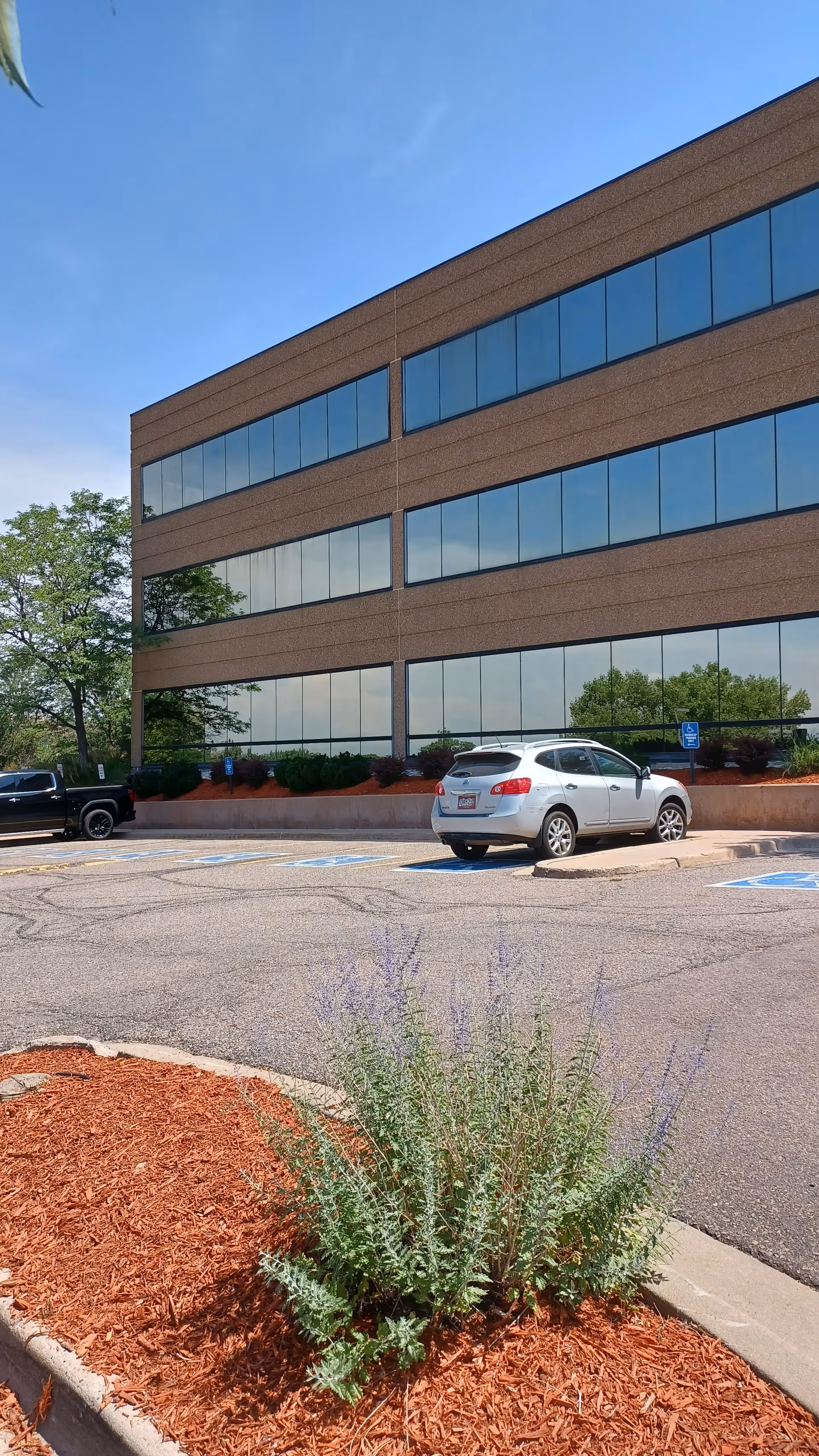 Exterior view of a brick office-style building with large blue-glass windows and parked cars.