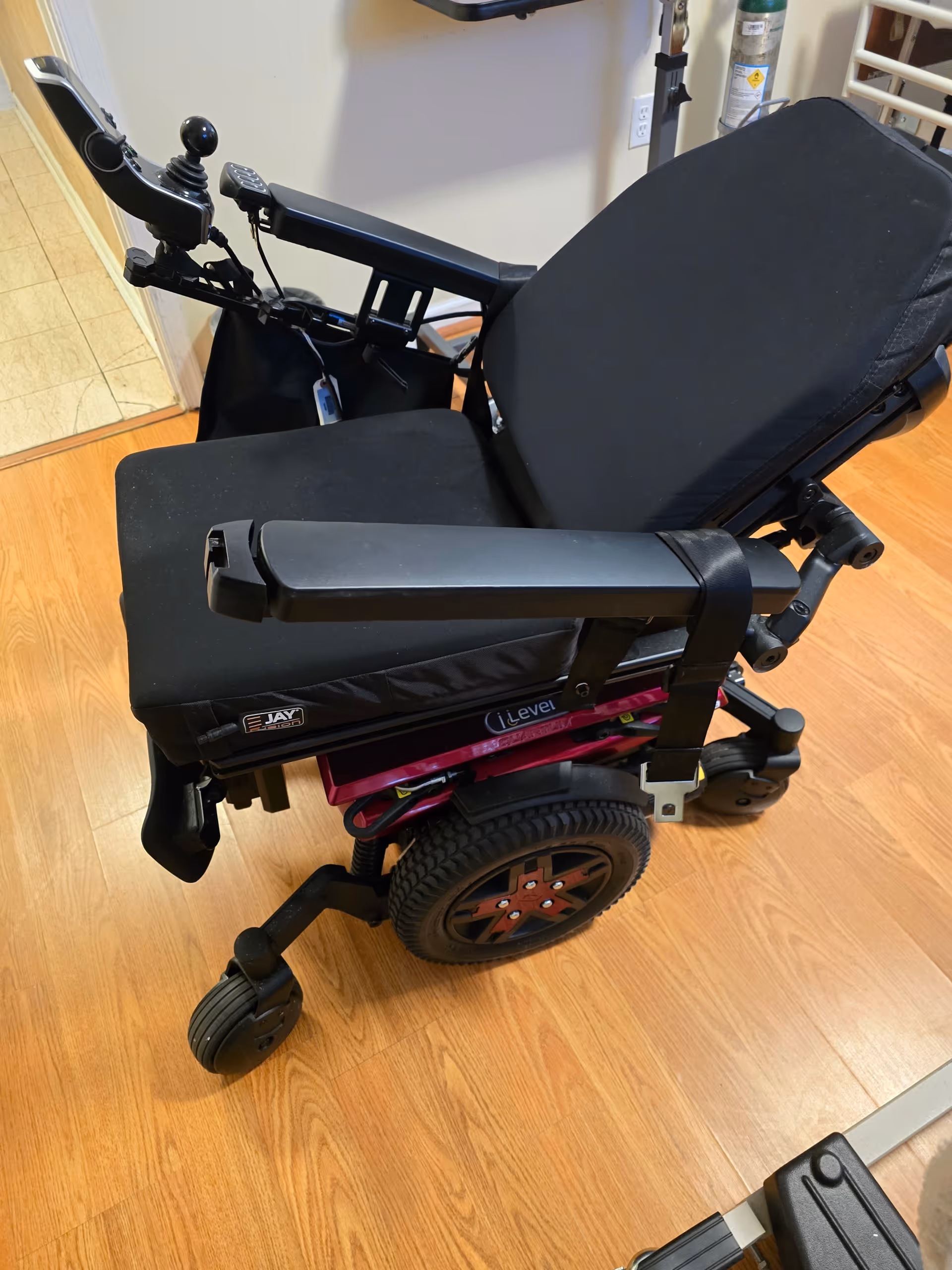 Black wheelchair on wood floor in an indoor facility hallway.