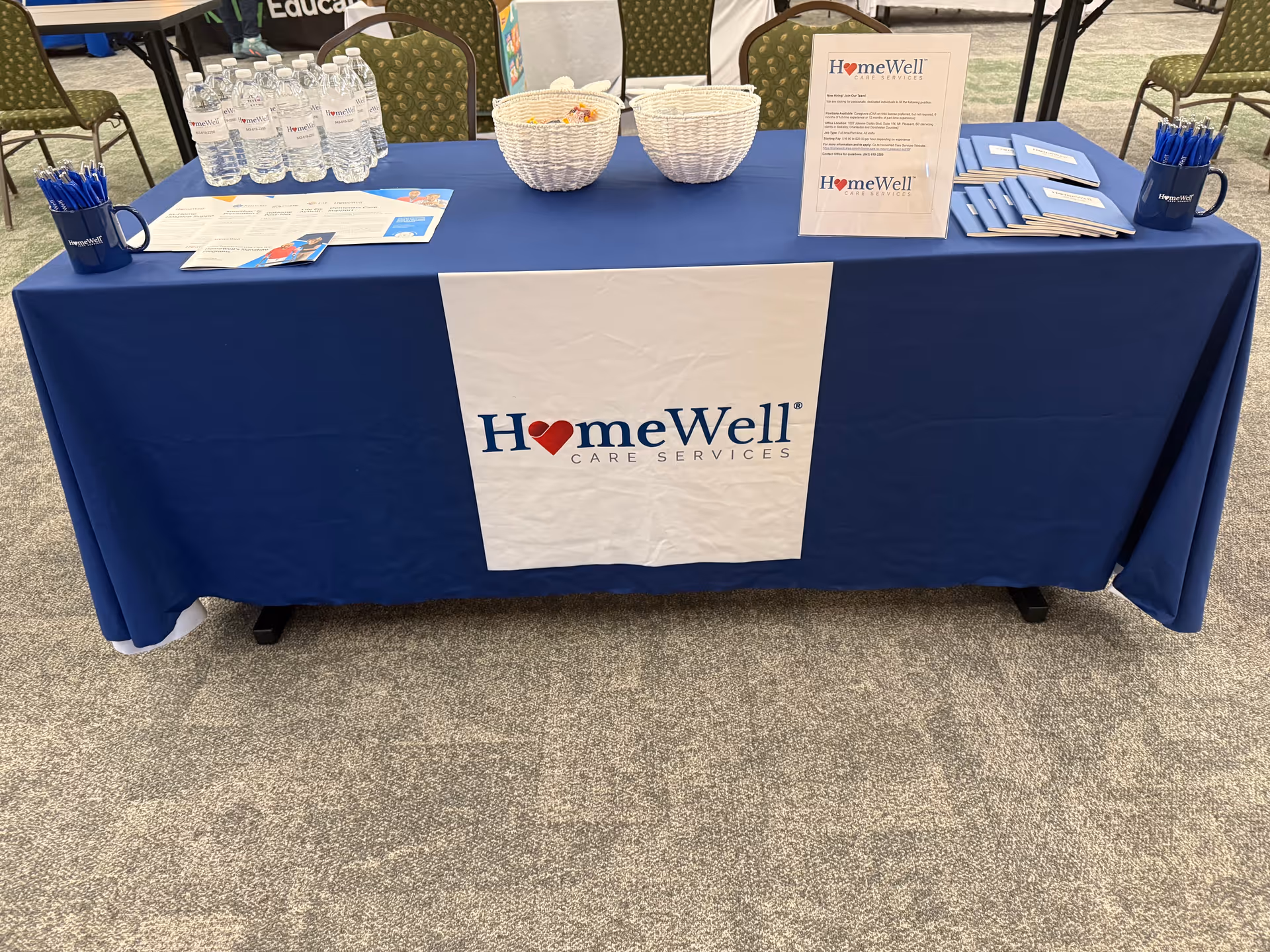 Blue table with HomeWell Care Services banner and brochures at an event.