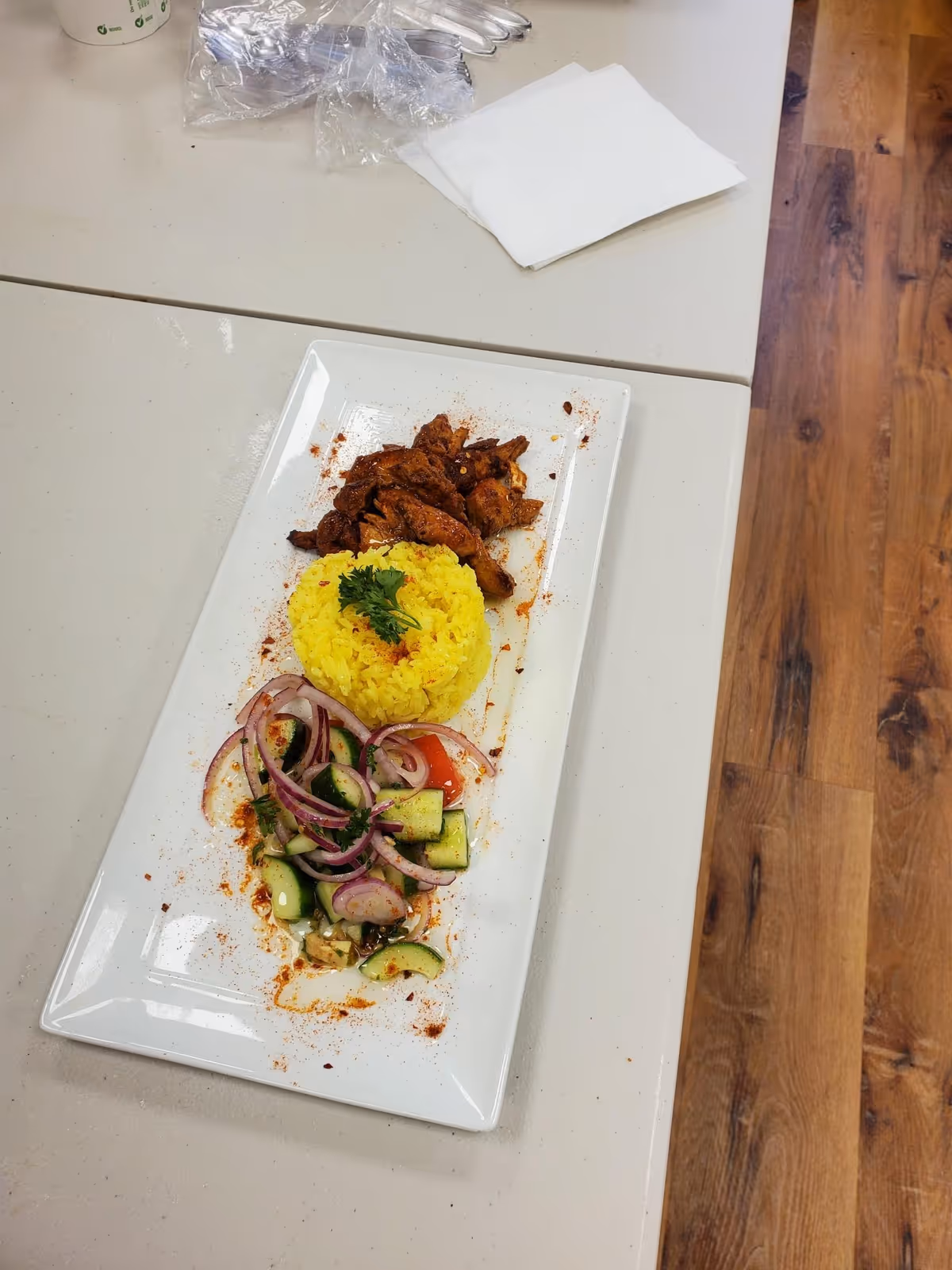 Plate of yellow rice with meat and cucumber-onion salad on a long white platter.