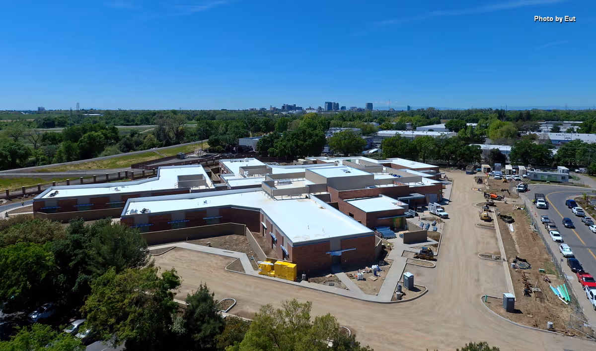 Aerial view of a large brick building complex under construction with dirt roads and equipment.
