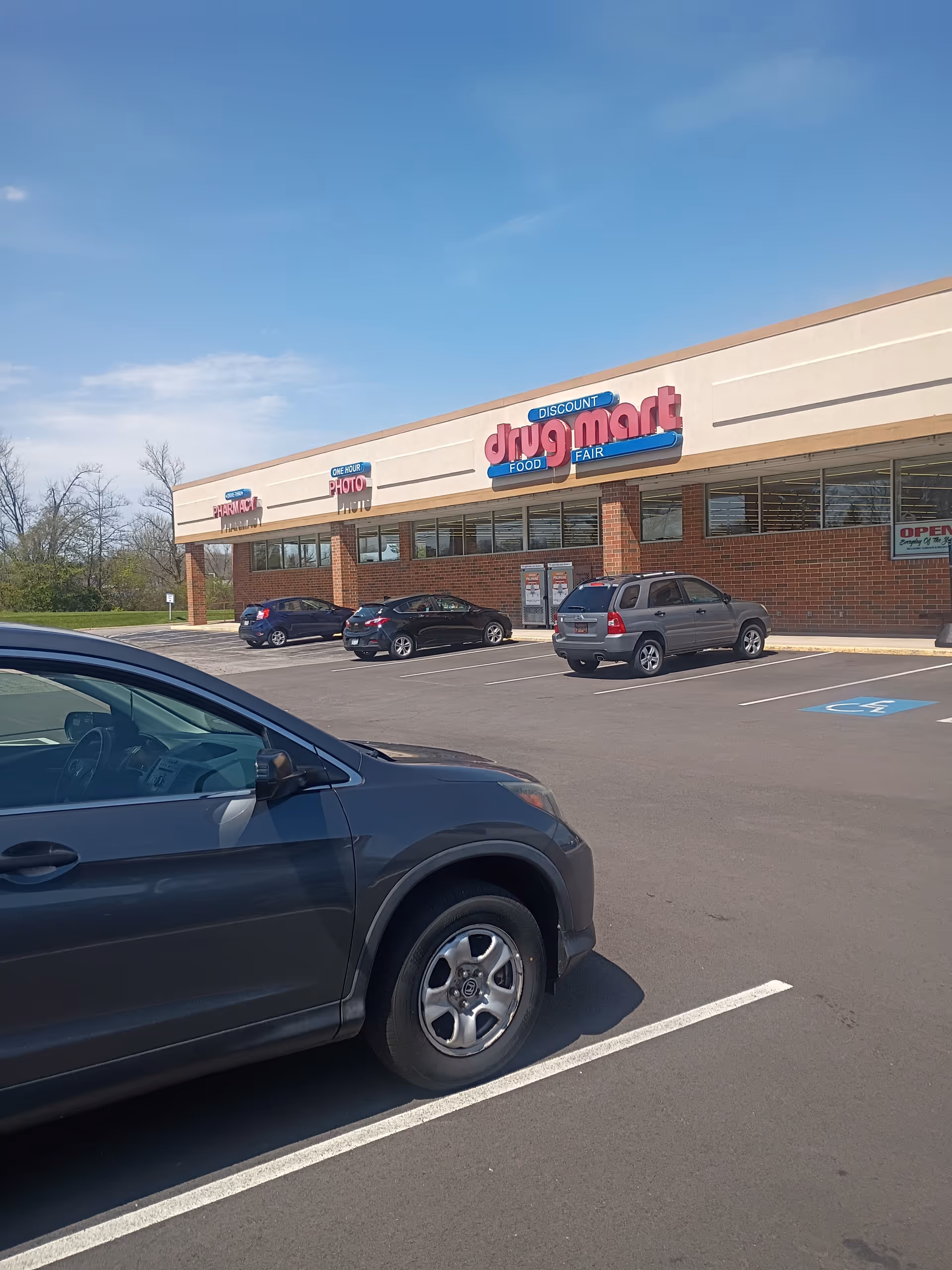 Parking lot in foreground with Discount Drug Mart storefront and clear blue sky.