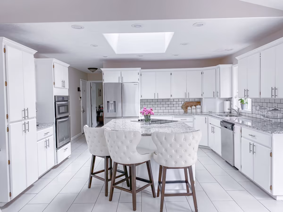 Bright white kitchen with island, marble countertops, and stainless appliances.