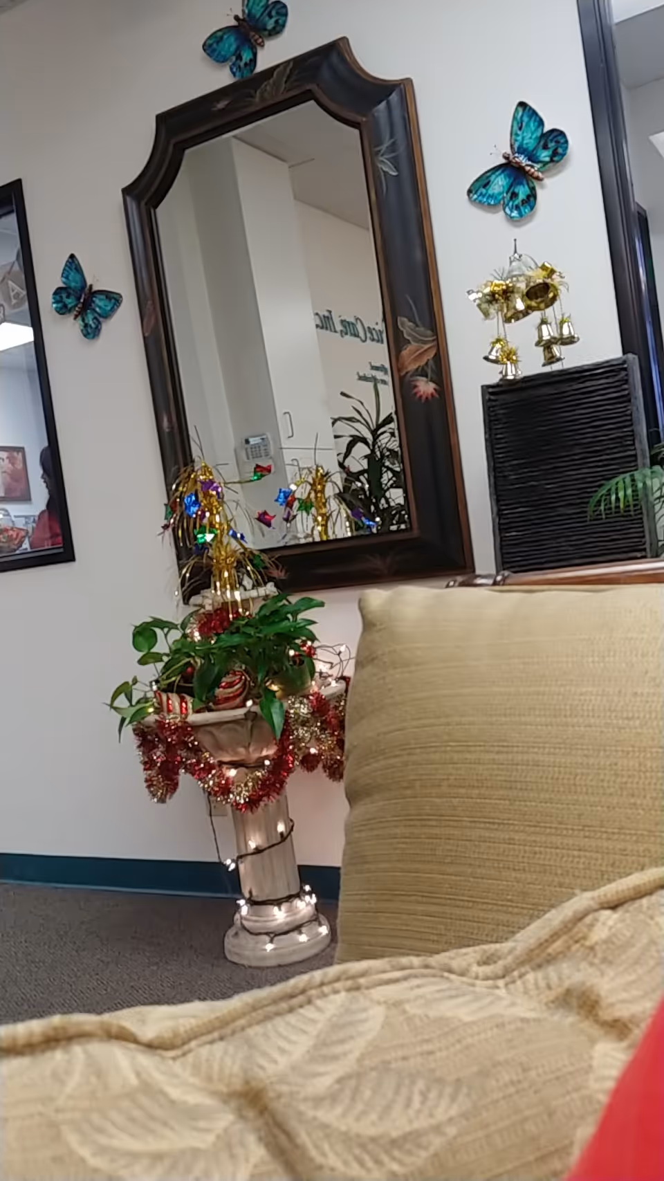 Interior lounge with a large mirror, butterfly wall decor, plants, and a beige sofa.