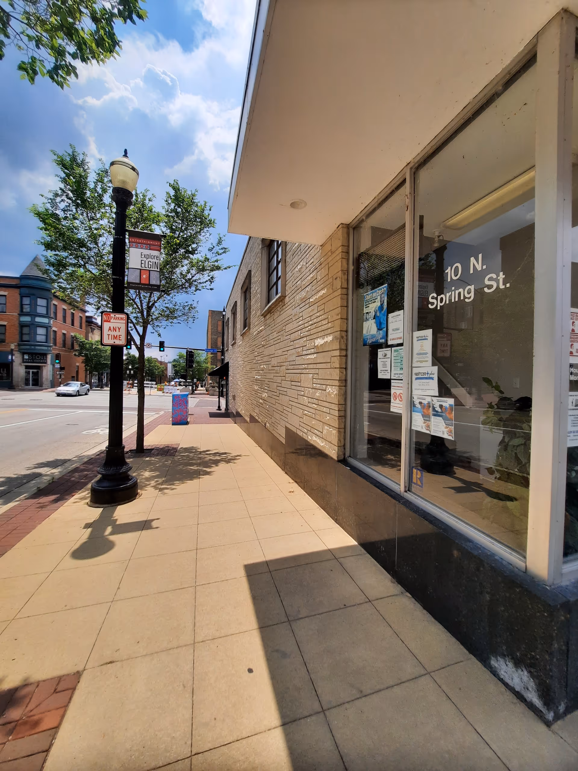 Sunlit street view of a brick storefront with posters on its windows.