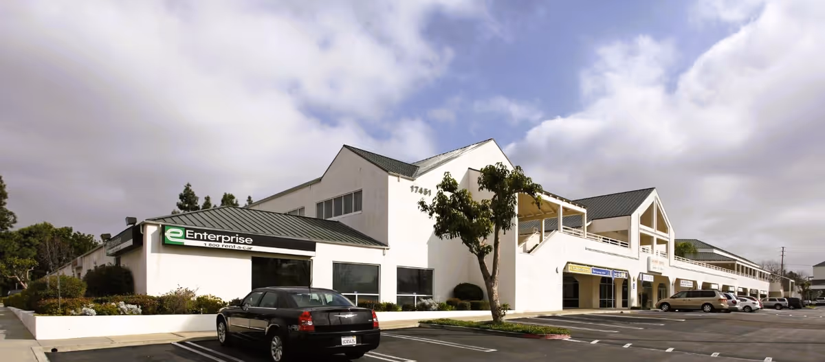 Exterior view of a white multi-tenant building with a parking lot and trees.