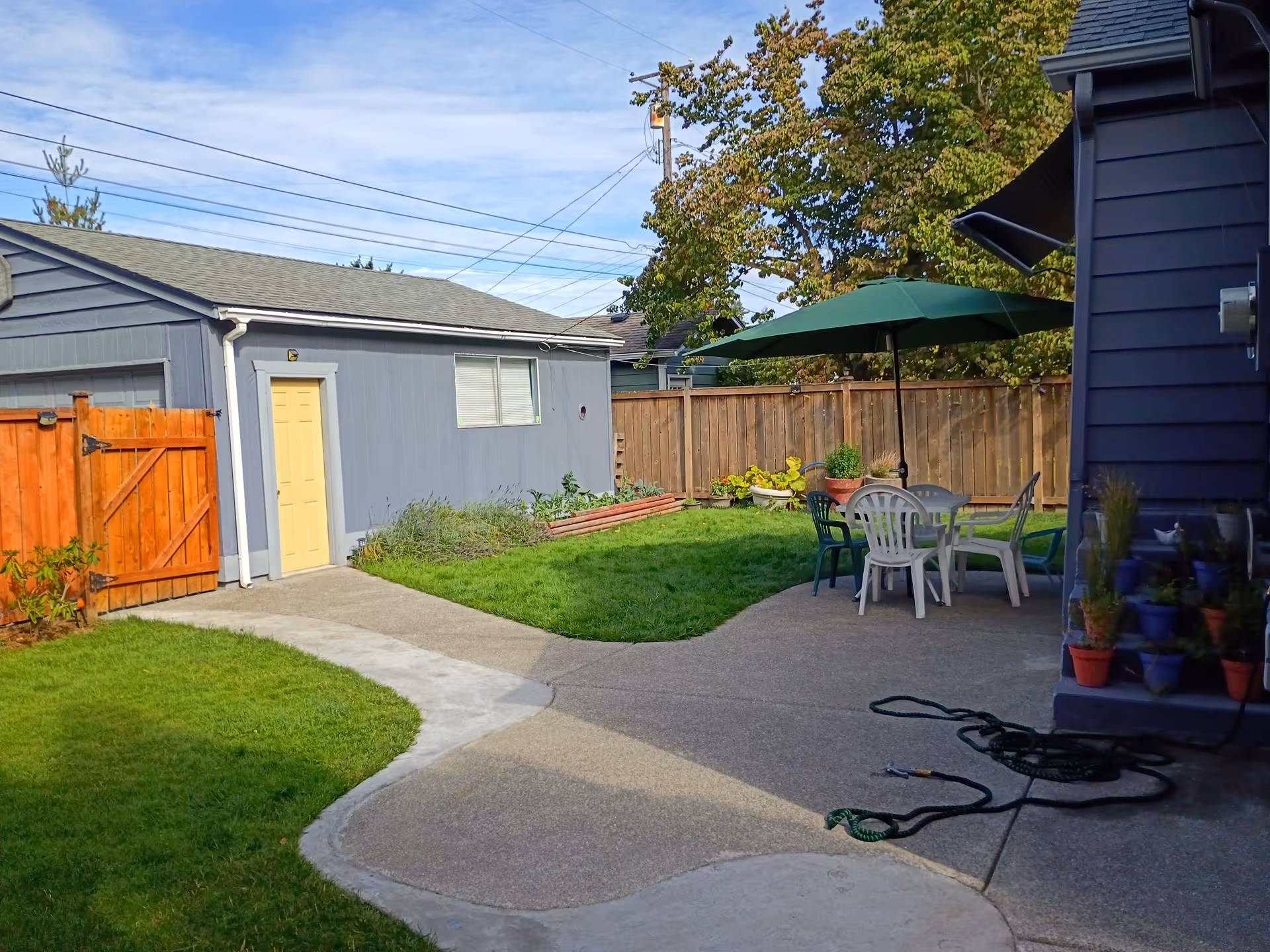 Backyard patio with outdoor table, chairs, umbrella, and fenced lawn area.