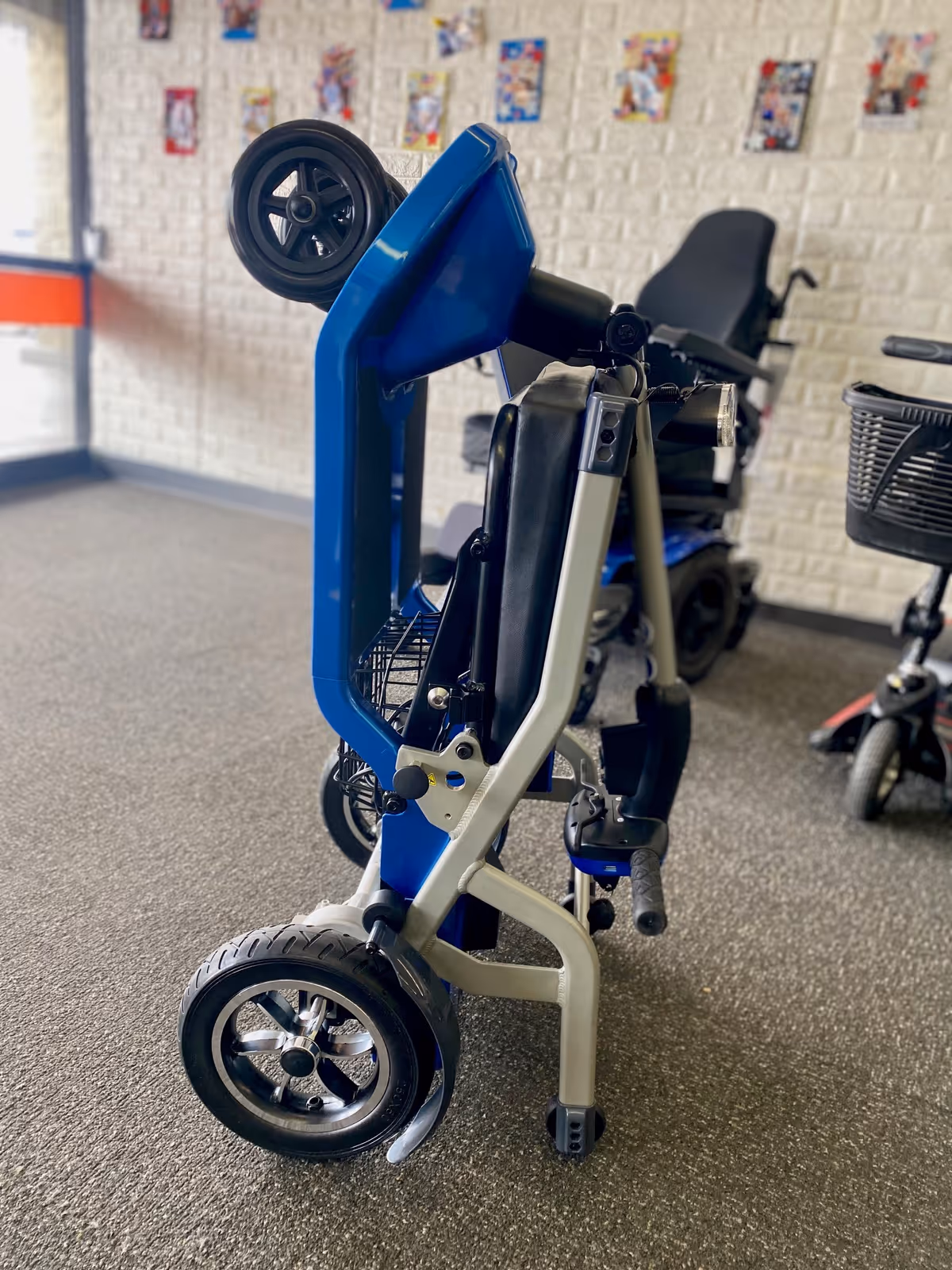 Blue folding wheelchair inside a senior facility hallway with posters on the wall.