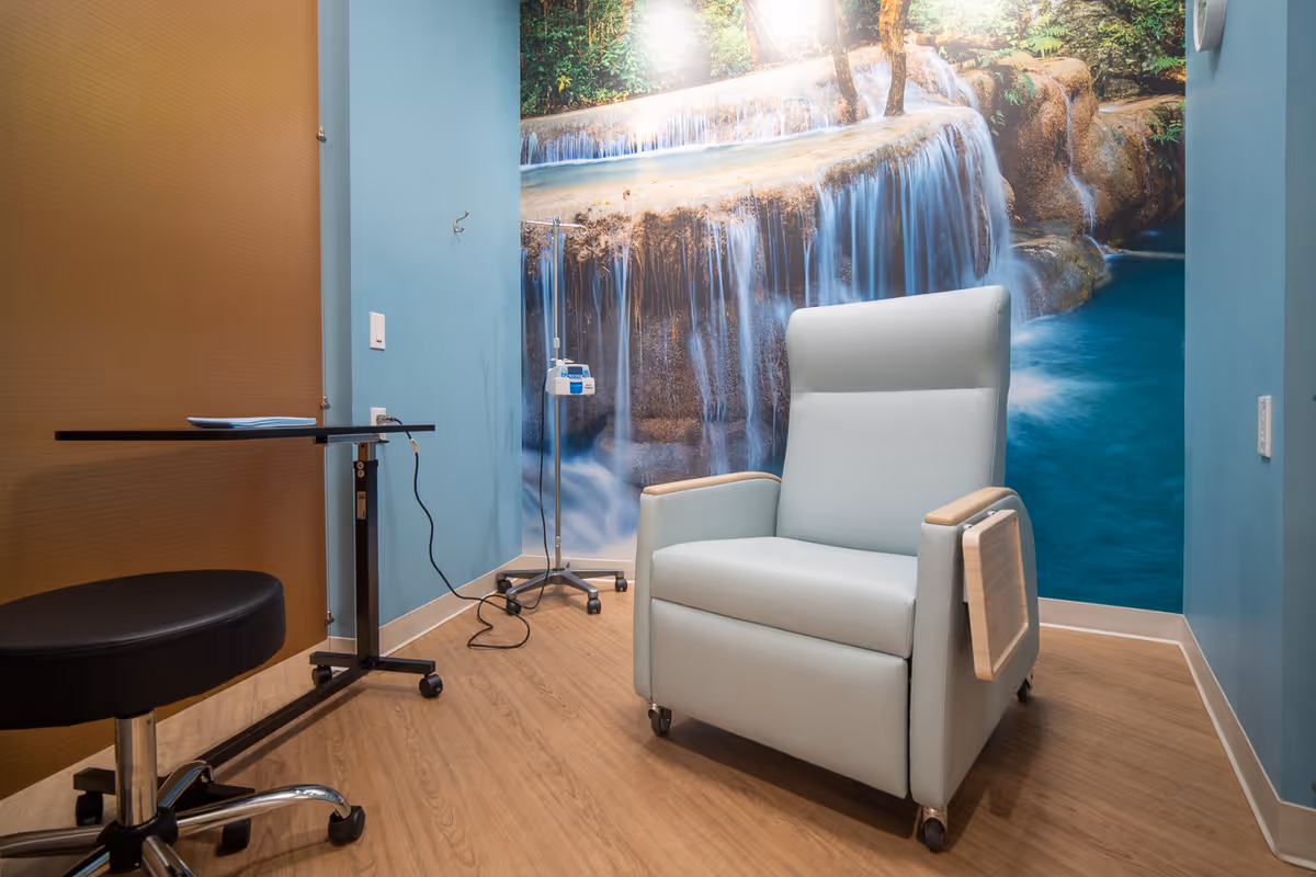 Blue infusion chair in a bright room with a waterfall mural and medical equipment.