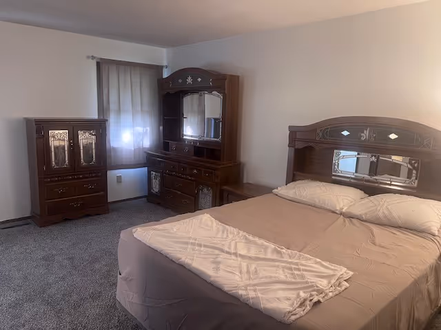 A furnished bedroom with a large bed, dresser, mirror, and nightstand.