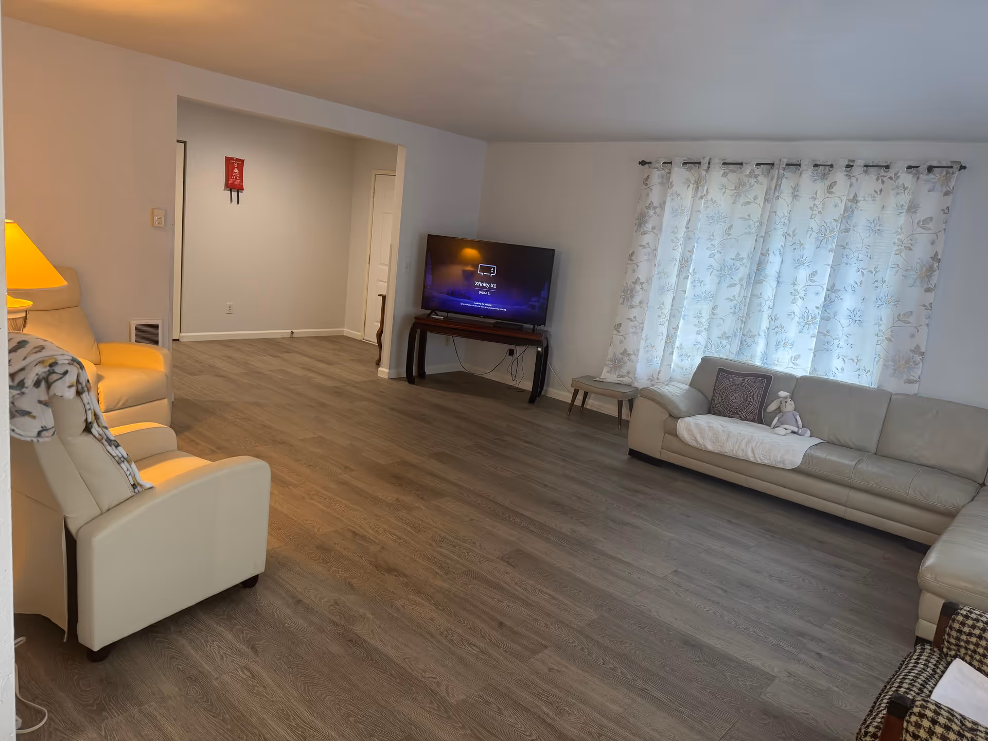 Spacious senior living room with leather sofas, a TV, and light patterned curtains.