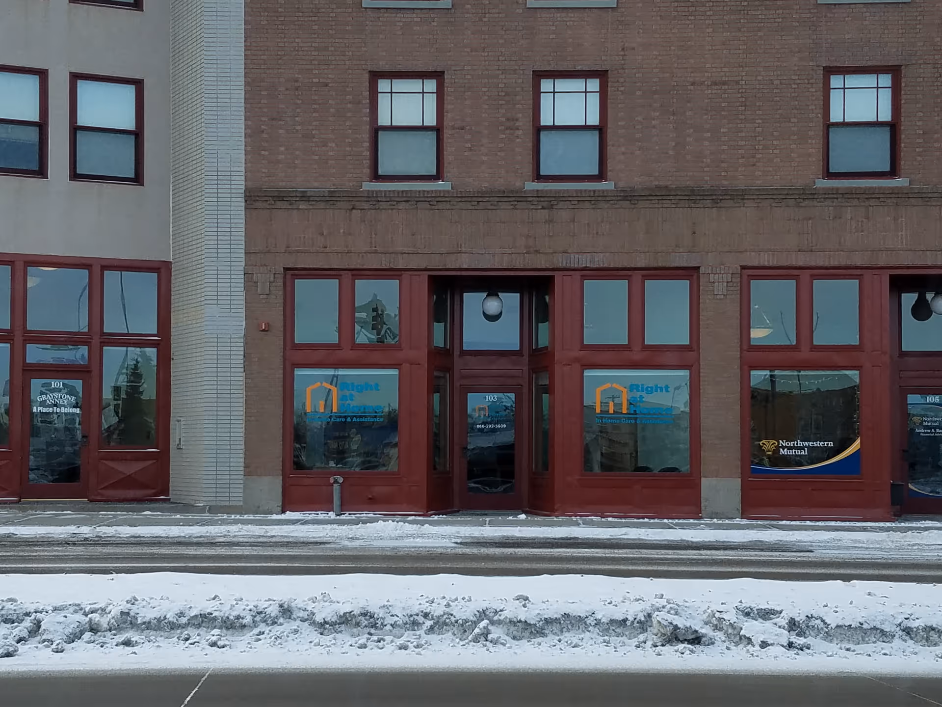 Brick building storefront with red-framed doors and windows displaying Right at Home signage.