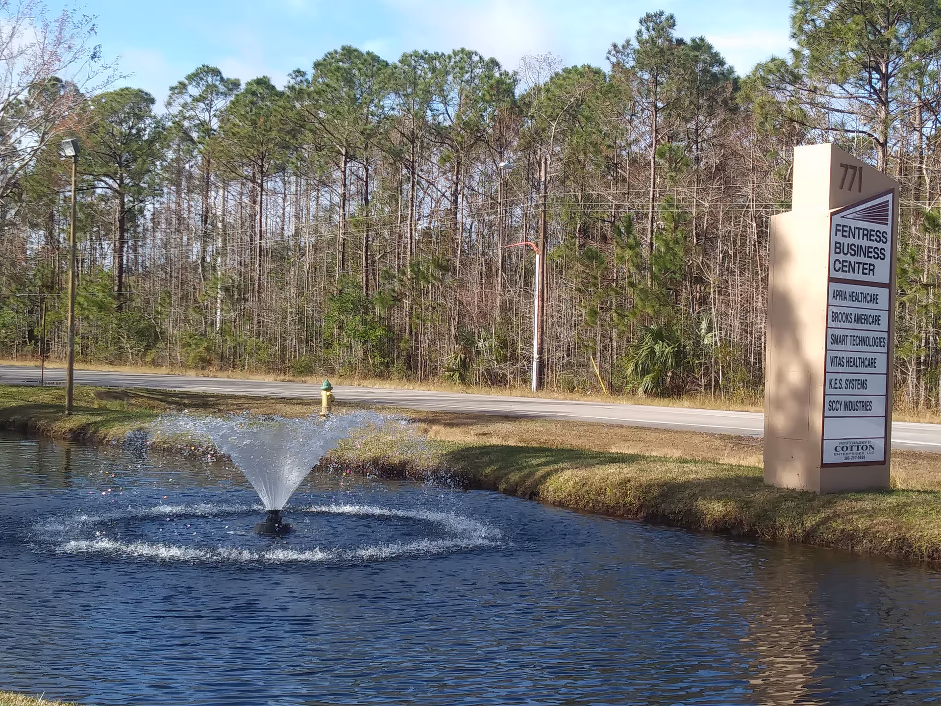 Exterior view of a pond with fountain and a tall sign along a road.