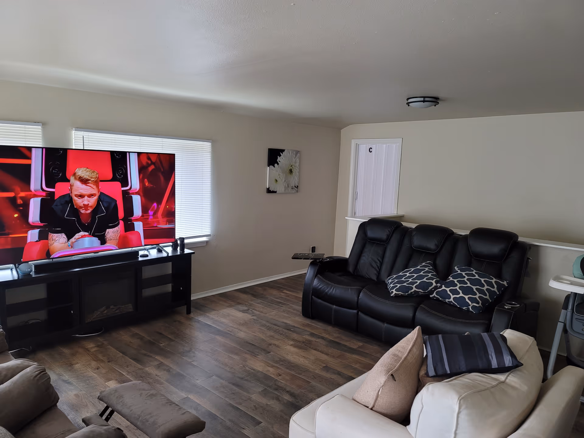 Living room in a senior facility with a large TV, black leather sofa, and beige seating.