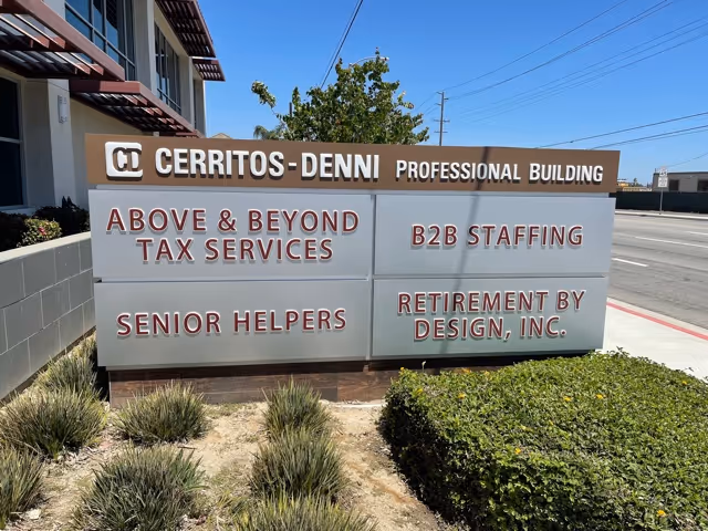 Exterior view of a building signboard listing tenants, including Senior Helpers, on the sidewalk.