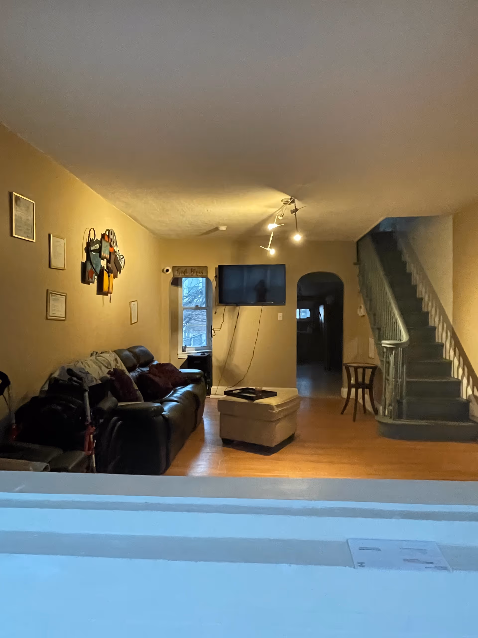 Cozy living room with leather sofa, ottoman, wall-mounted TV, staircase, and wall decor.