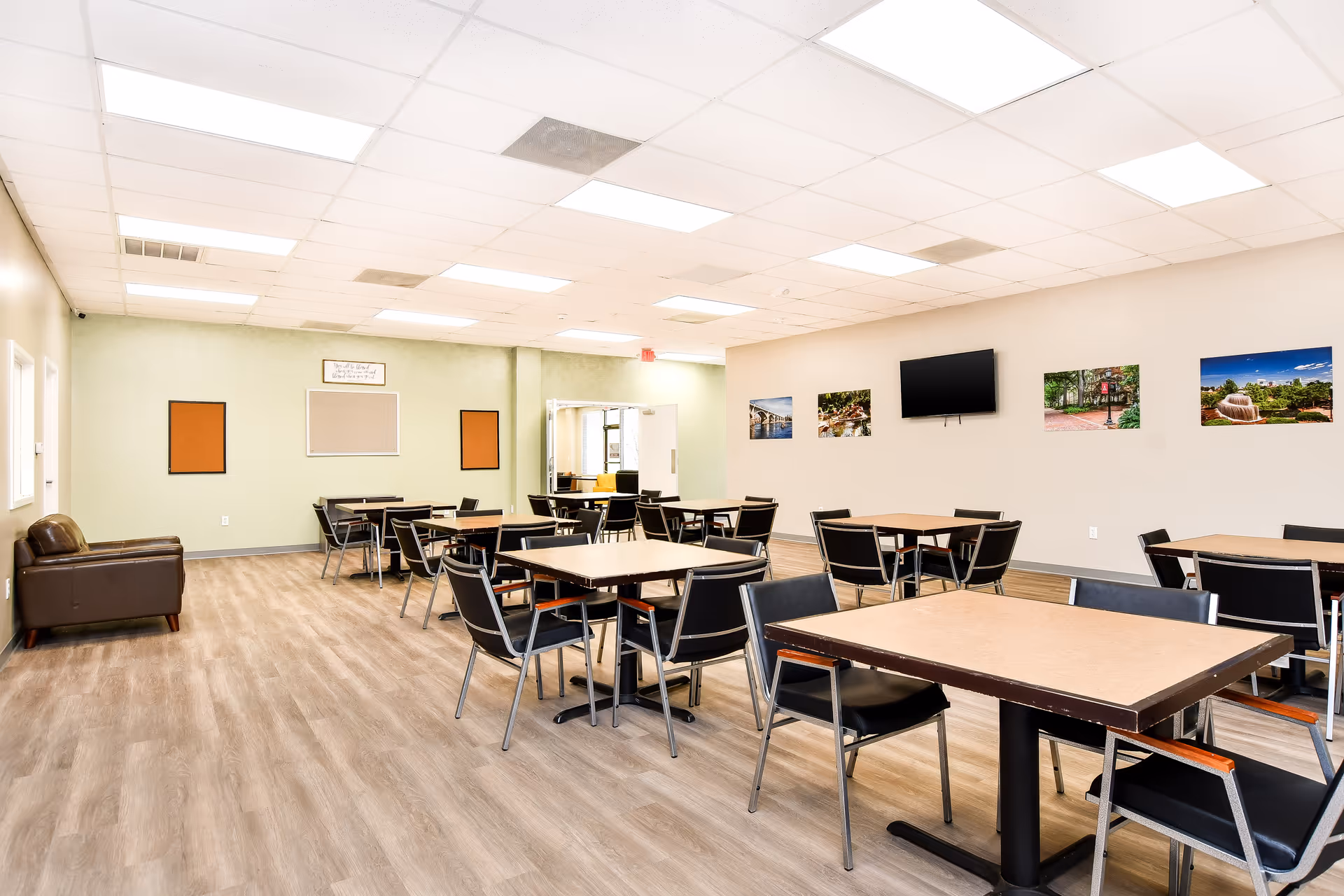 A spacious dining room with several tables and chairs, wall-mounted photos, and a TV.