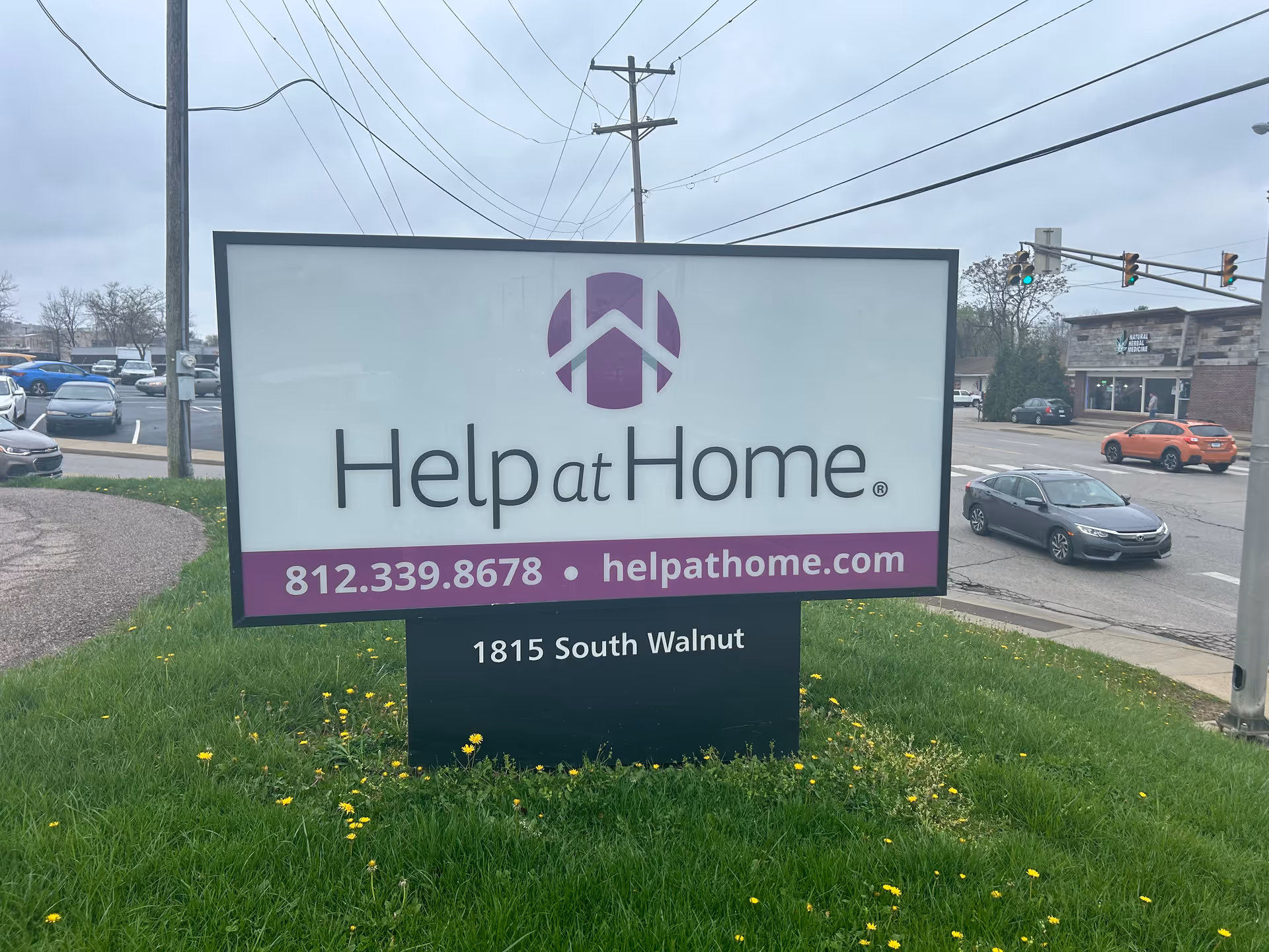 Help at Home senior living sign on a grassy median beside a busy street.