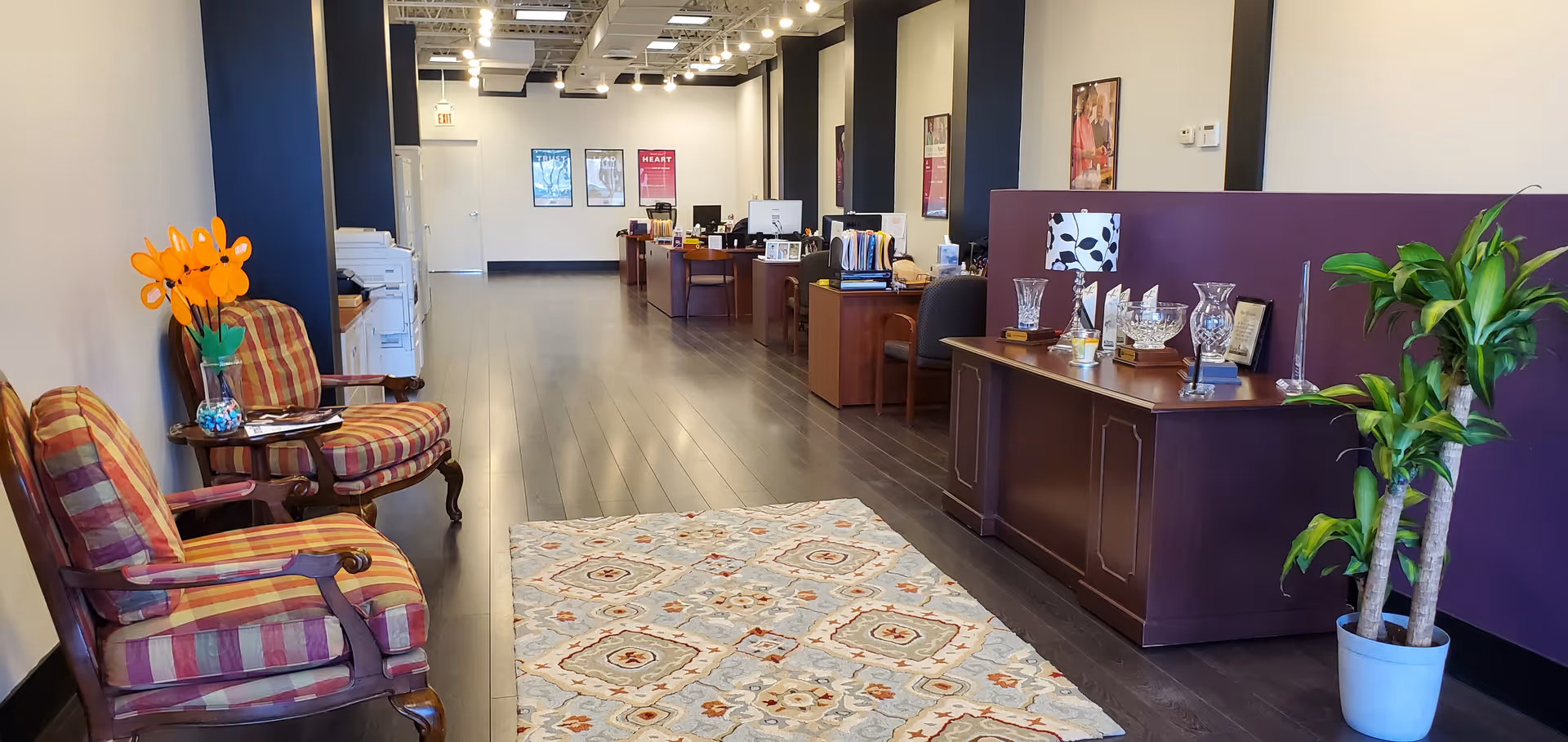 A spacious reception lobby in a senior living facility with dark wood desks and plants.