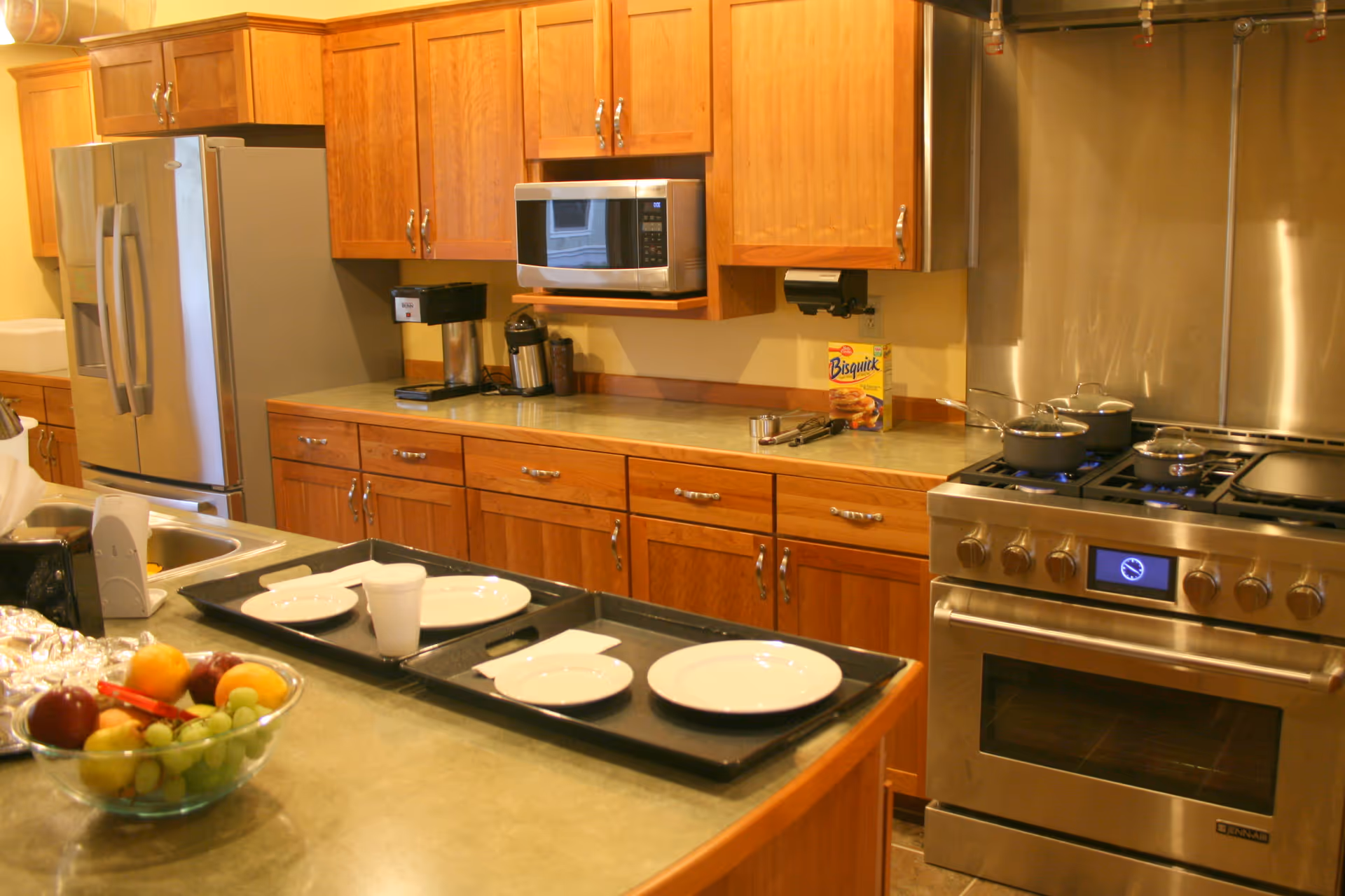 Bright kitchen with stainless steel appliances, wooden cabinets, and a fruit bowl on the island.