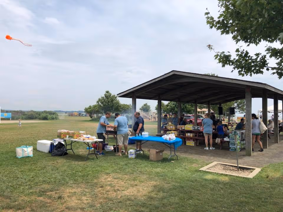 Outdoor pavilion hosts volunteers serving food to seniors at a park-like community event.