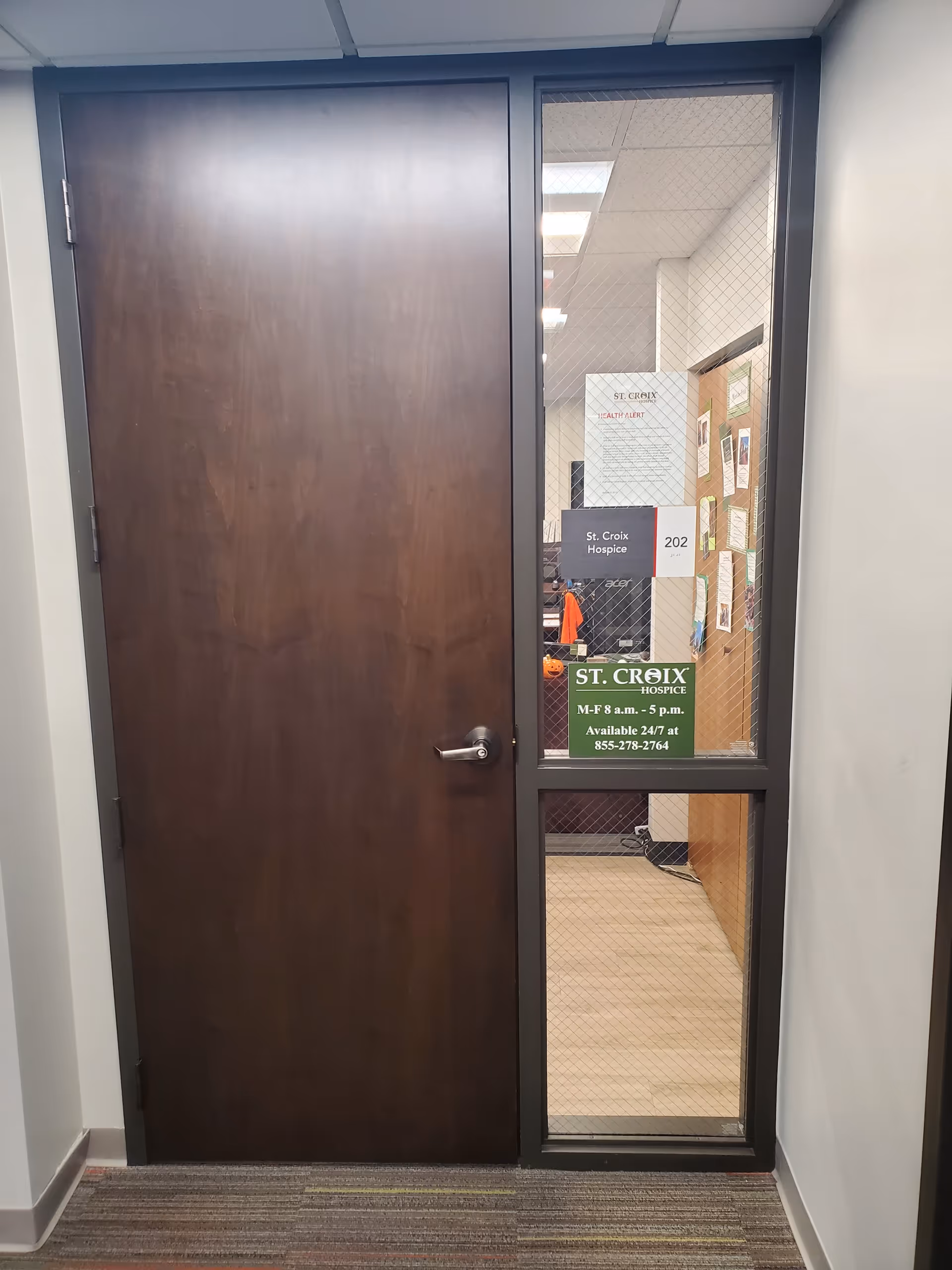 A wooden door beside a glass panel leads into a St. Croix Hospice office hallway.