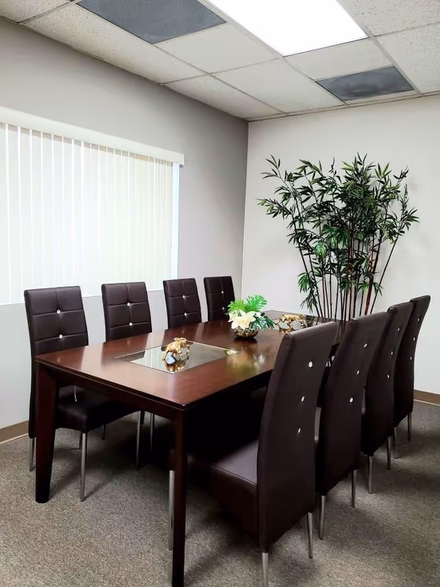 A wood conference table with brown chairs in a bright meeting room with a plant.