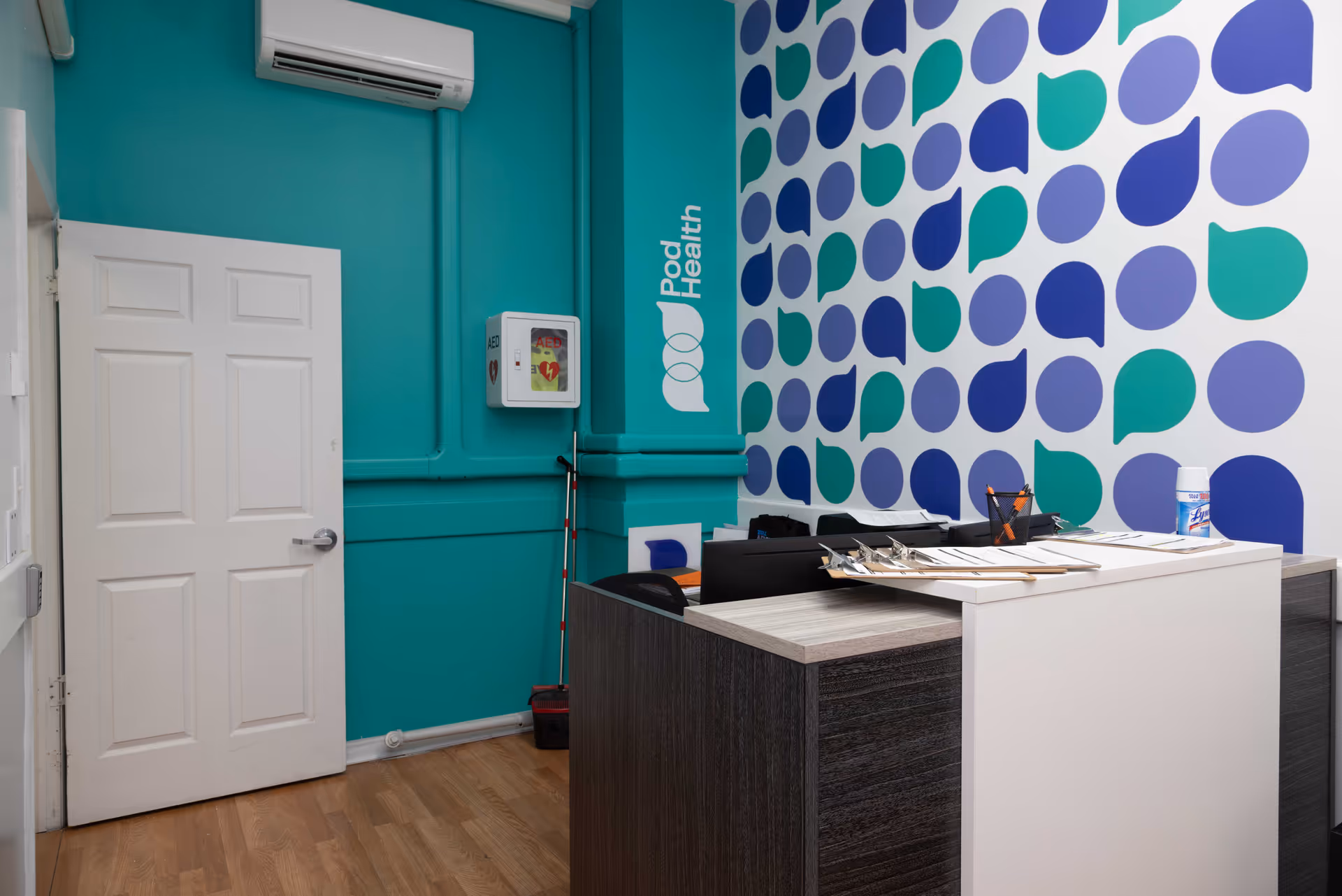 Reception desk in a colorful Pod Health interior with teal walls and geometric wallpaper.