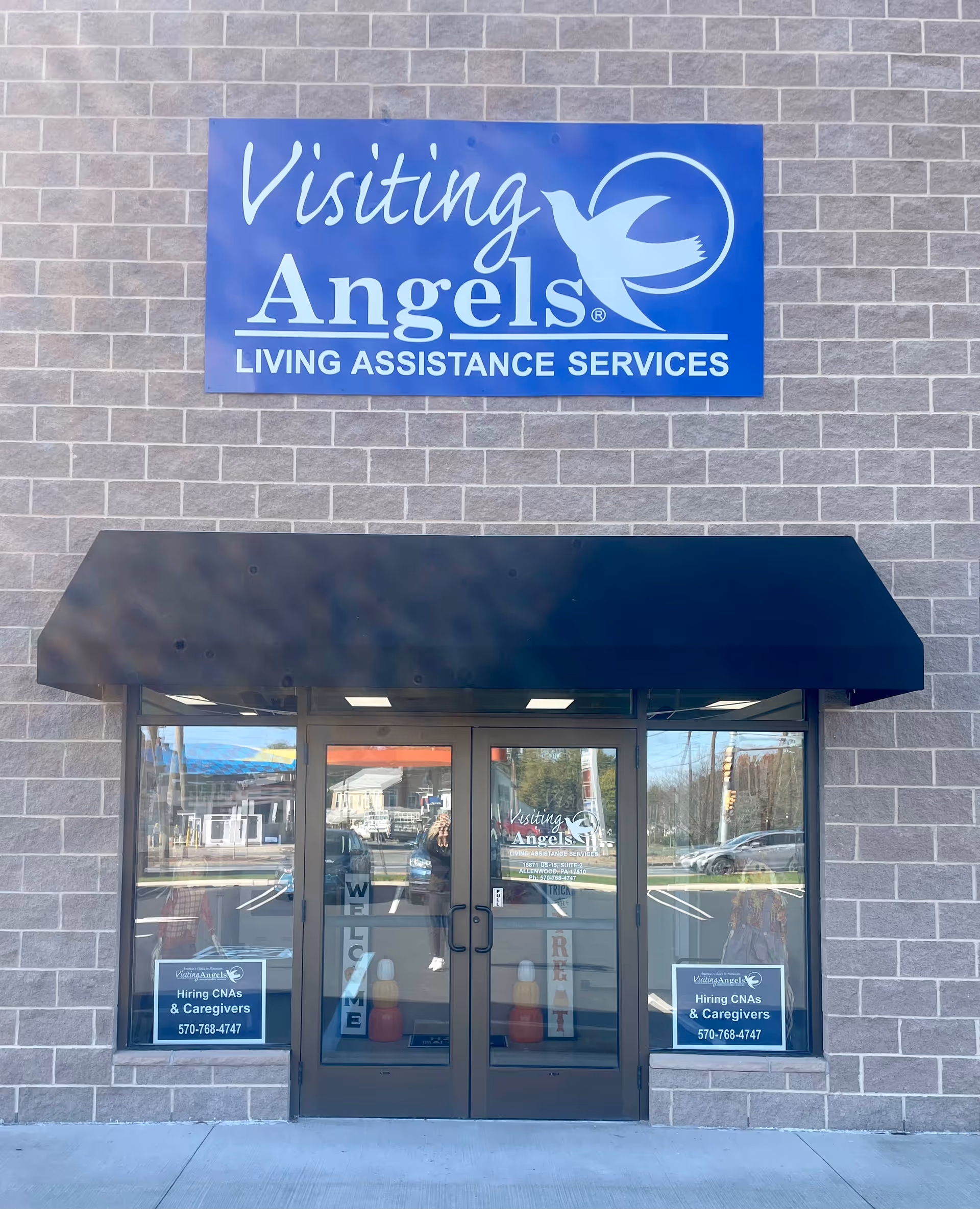 Blue Visiting Angels sign above glass doors on a brick building exterior.