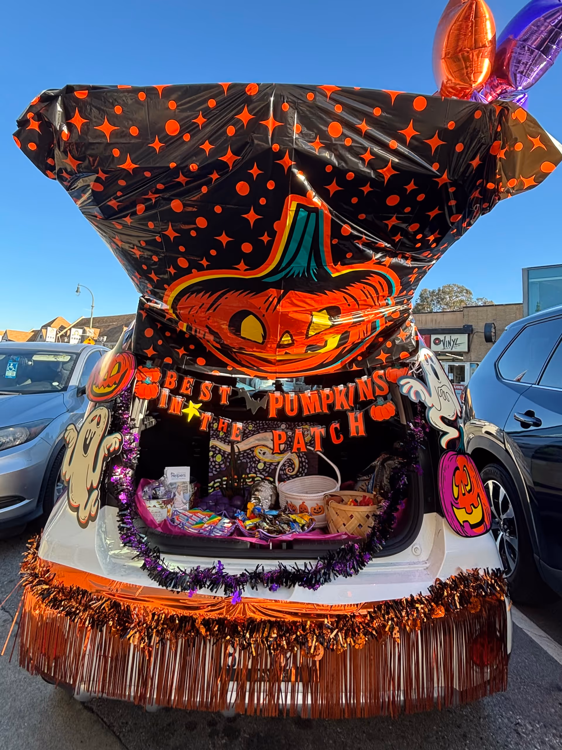 Decorated Halloween-themed car trunk open in a parking lot with pumpkins and candy