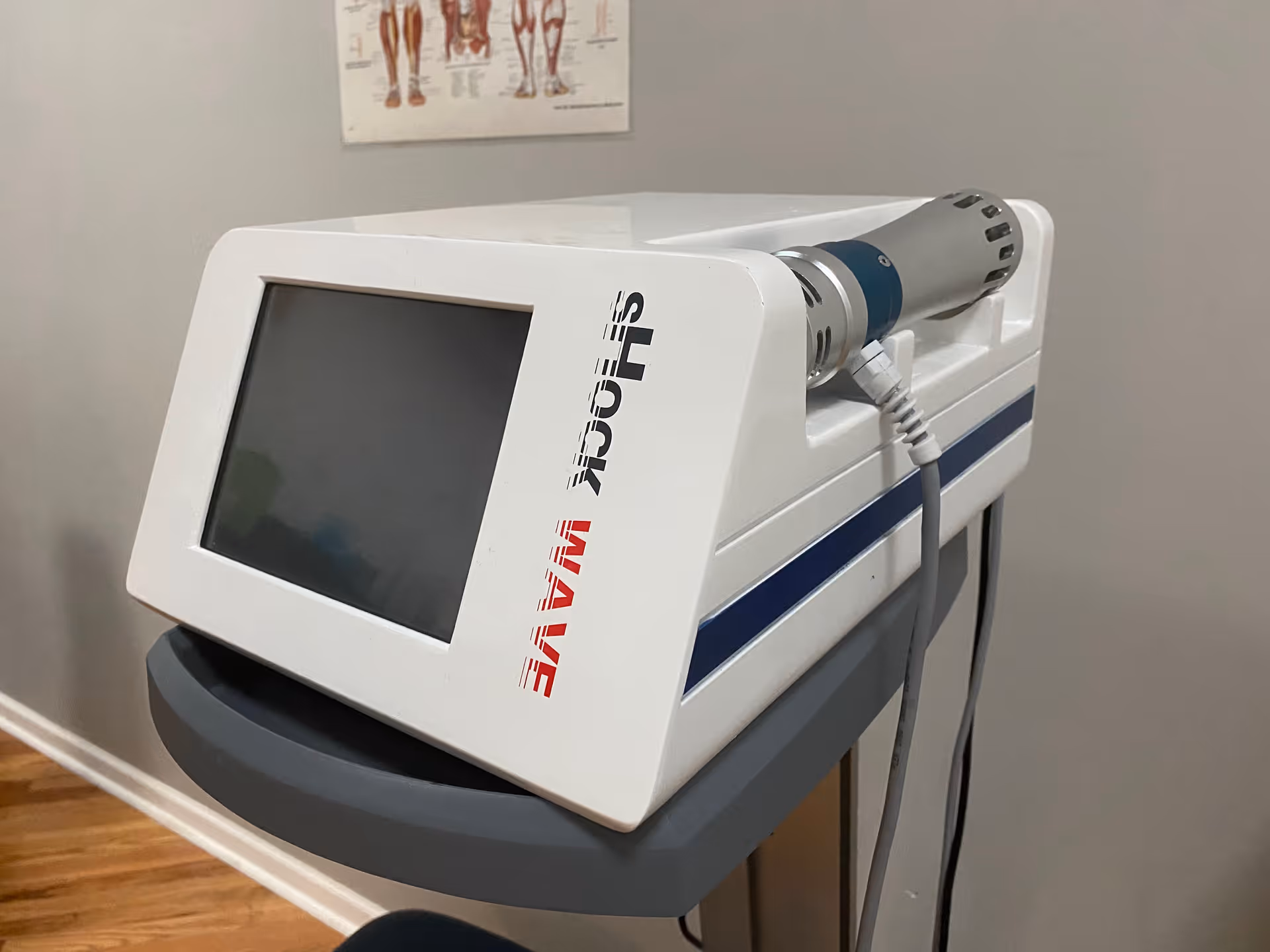 White medical device with touchscreen on a gray cart in an interior therapy room.