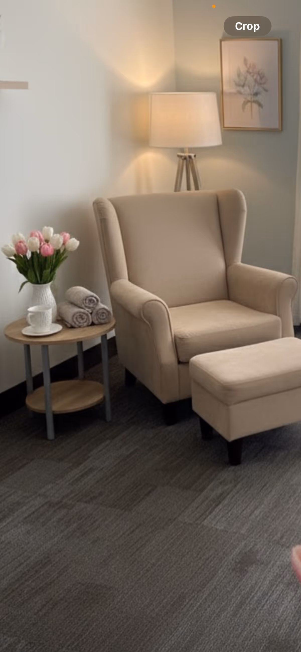 Cream armchair with ottoman beside a small table of flowers and towels in a cozy room.