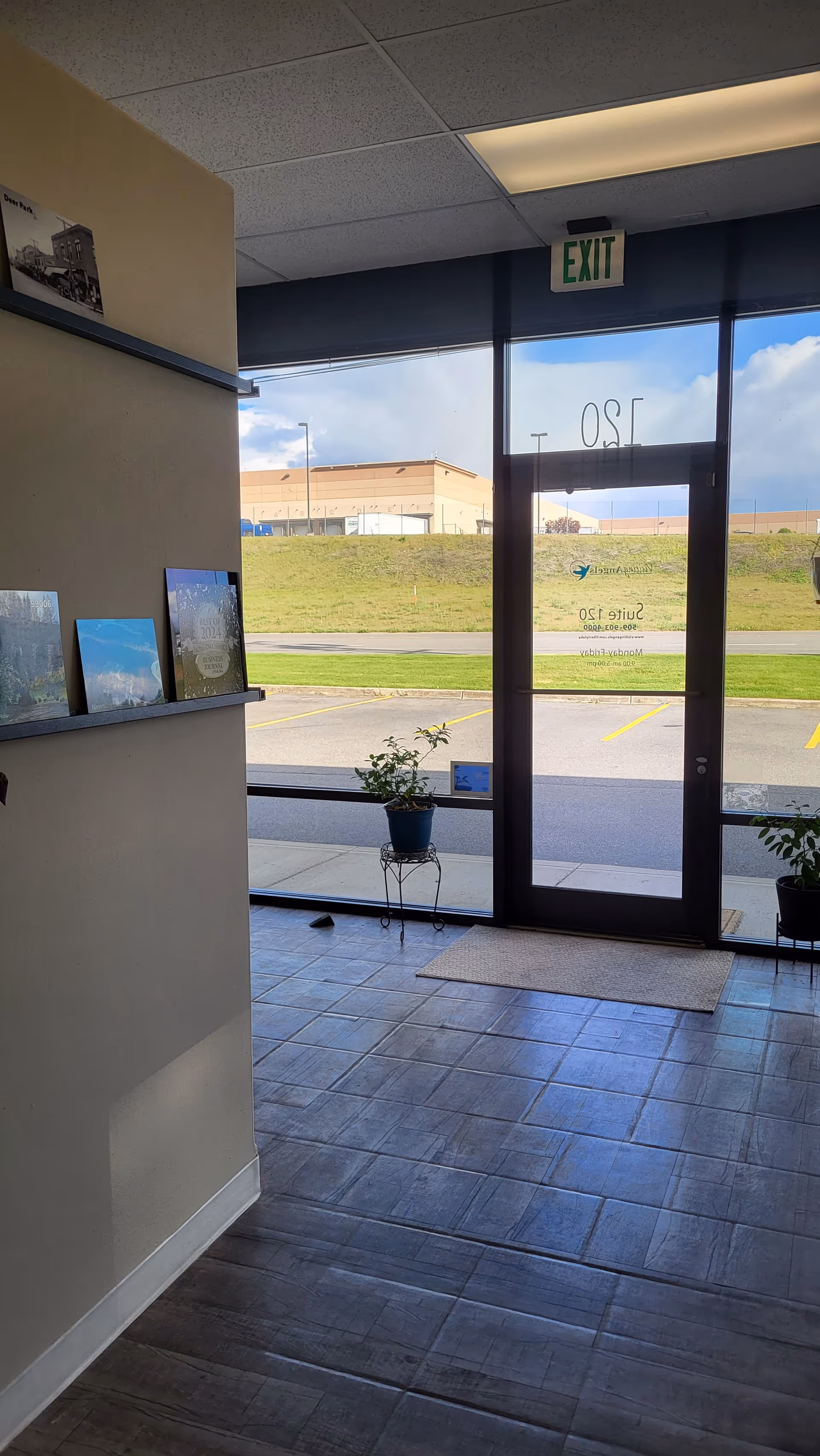 Interior entrance lobby with glass doors, exit sign, and potted plants.
