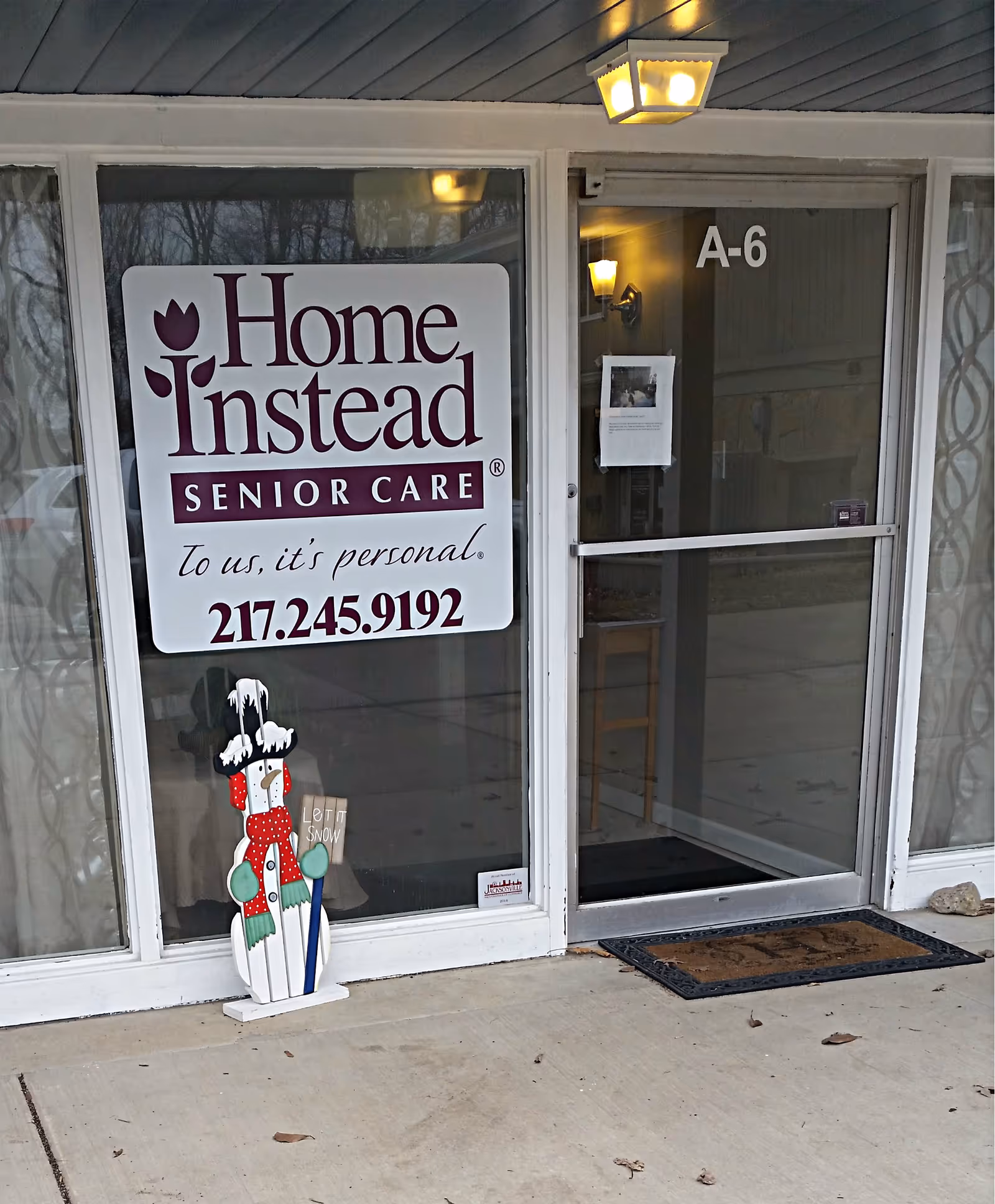 Home Instead Senior Care entrance with large sign on glass door and snowman decoration outside.