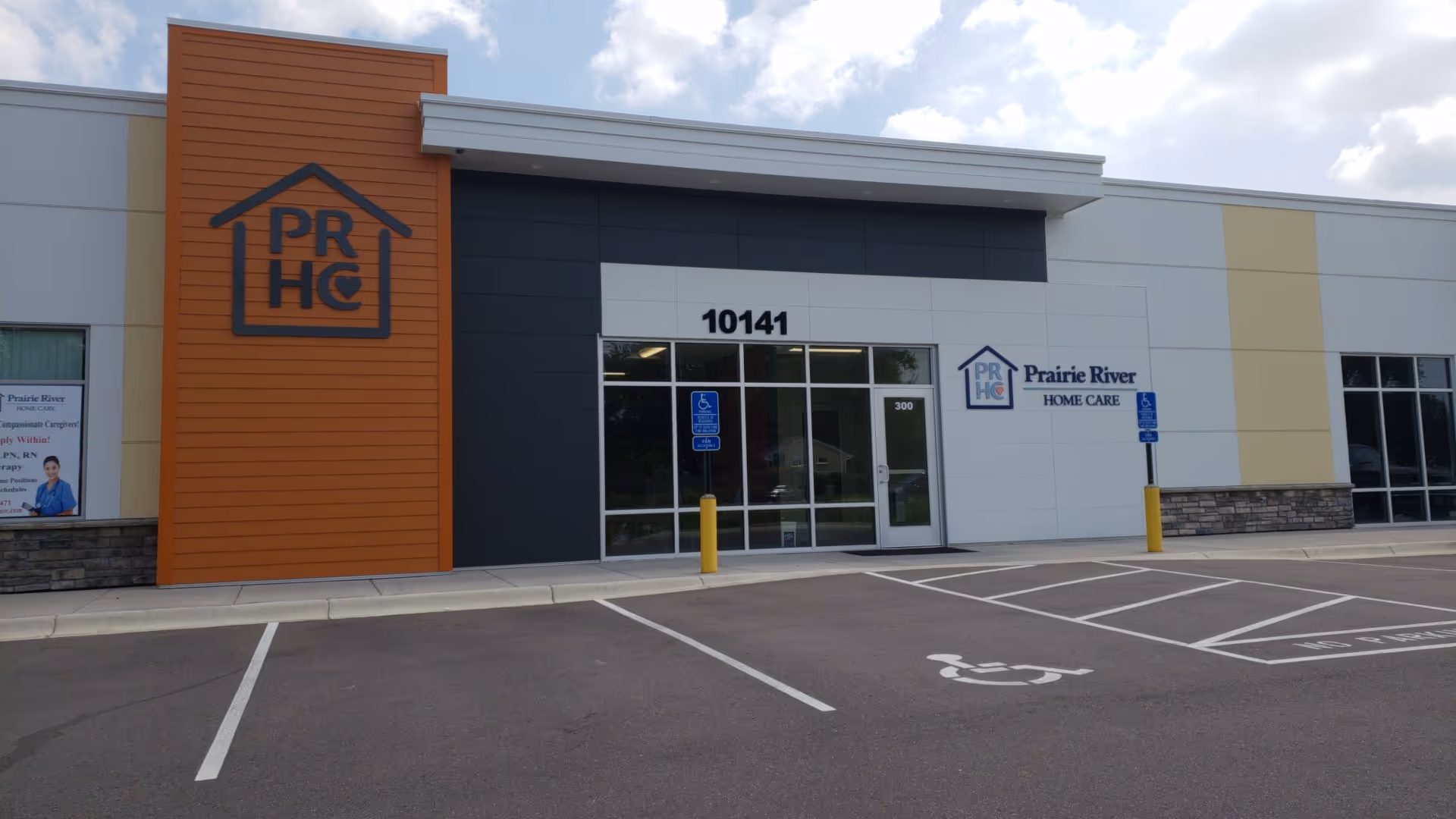 Exterior view of a care facility with a glass entrance and parking.