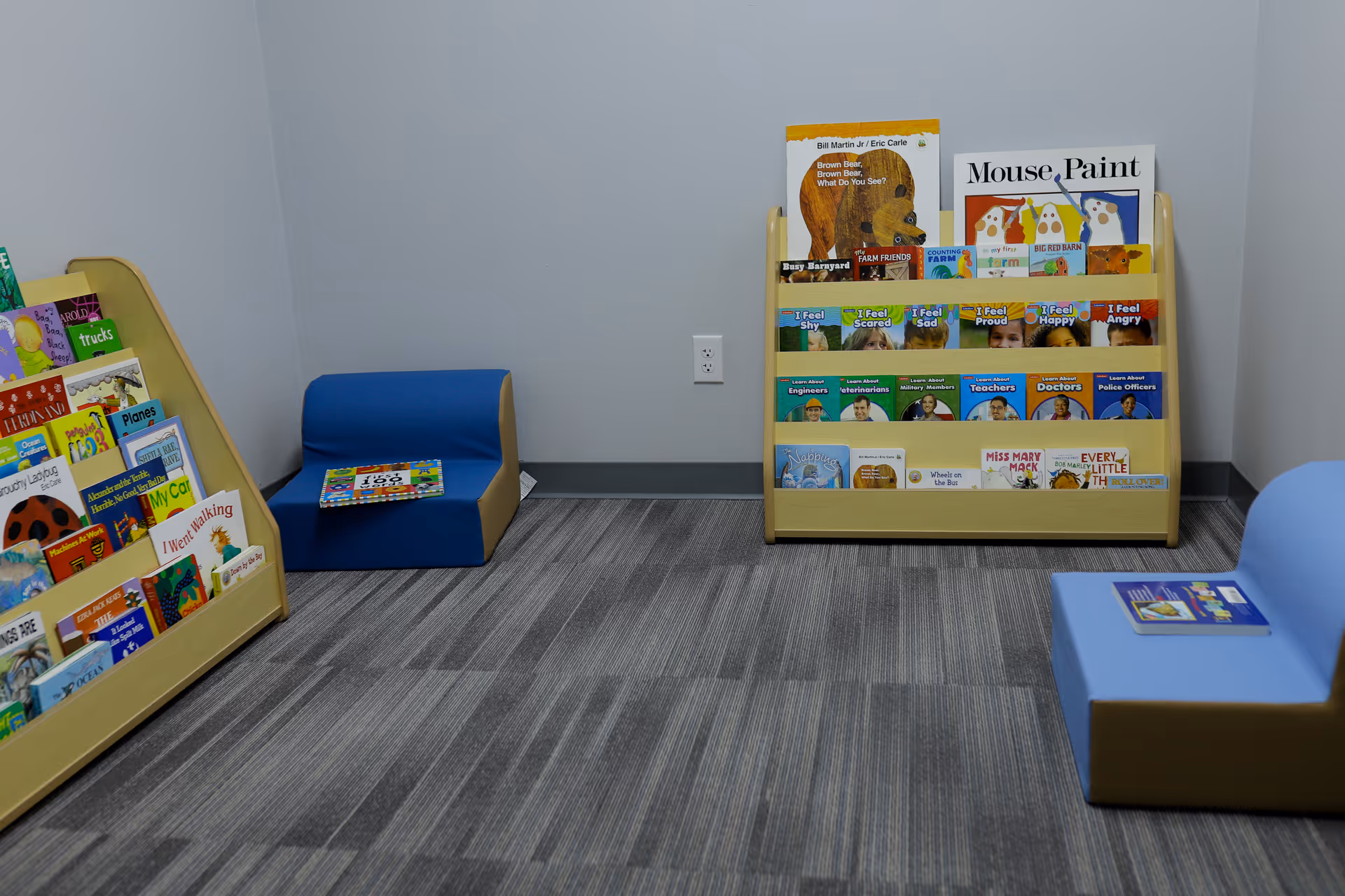 Bright children's reading area with low chairs, bookshelves, and a striped carpet.