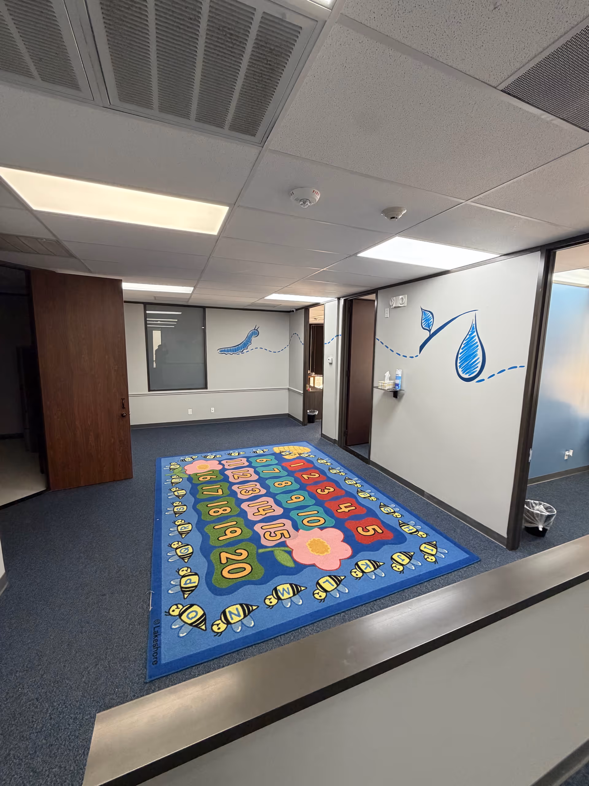 Interior hallway in a senior living facility with a colorful numbered rug and wall decals.