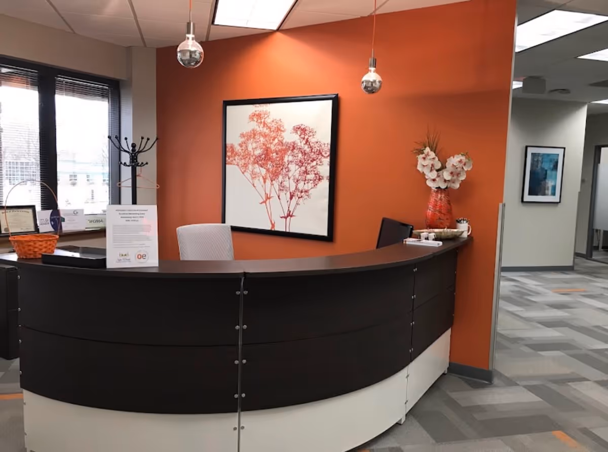 Curved dark reception desk in a lobby with an orange wall and art.