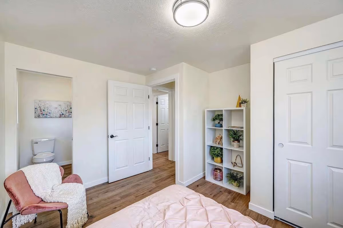 Light-filled bedroom featuring a pink bed, chair, and cube shelving unit.