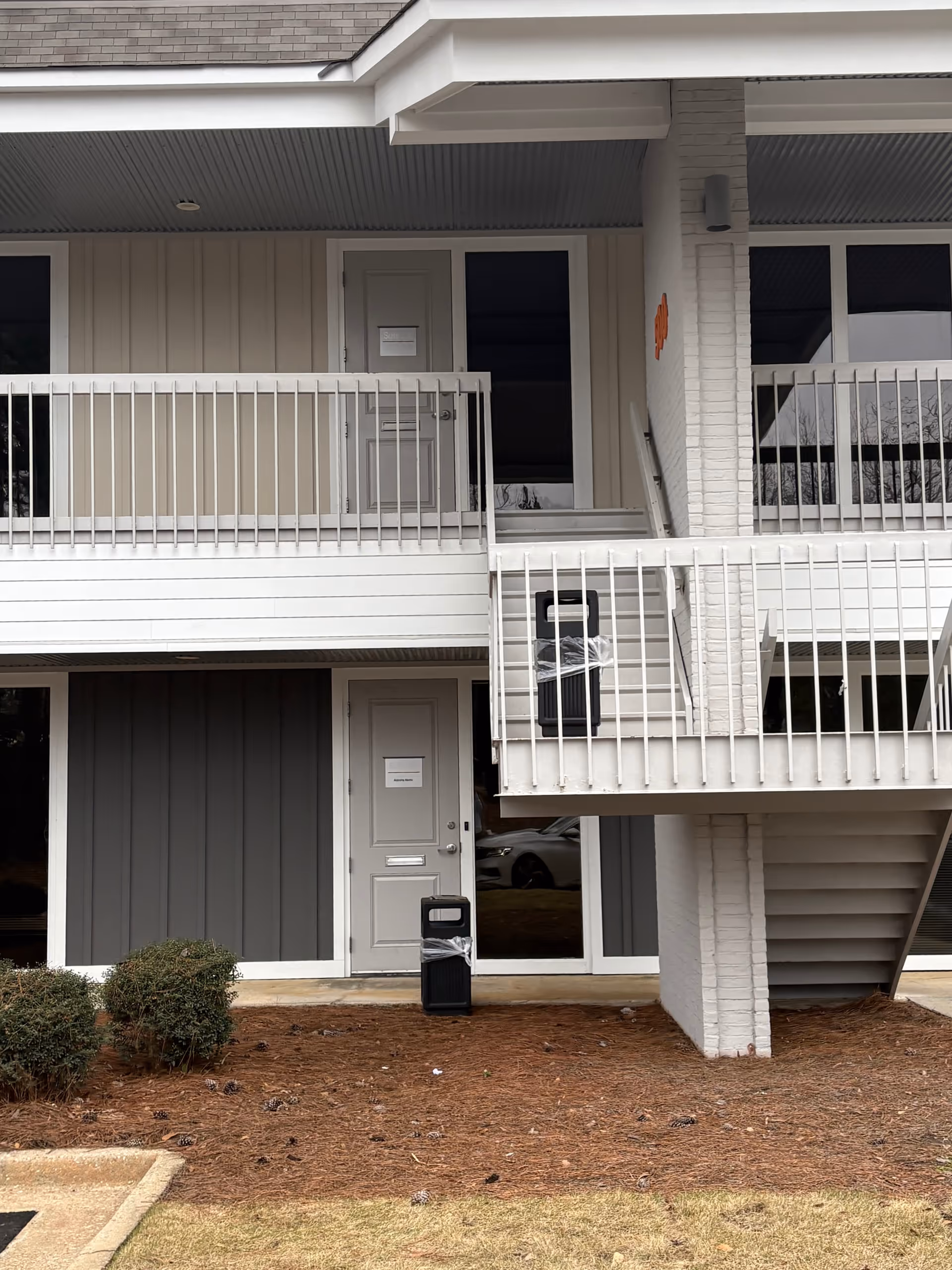 Exterior of a multi-unit building with doors, staircases, and white railings.