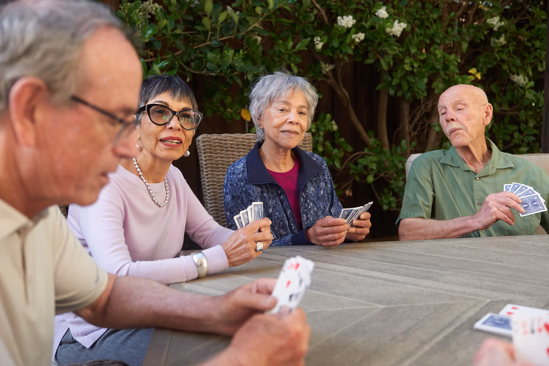 Four seniors sit around an outdoor table, playing cards together.