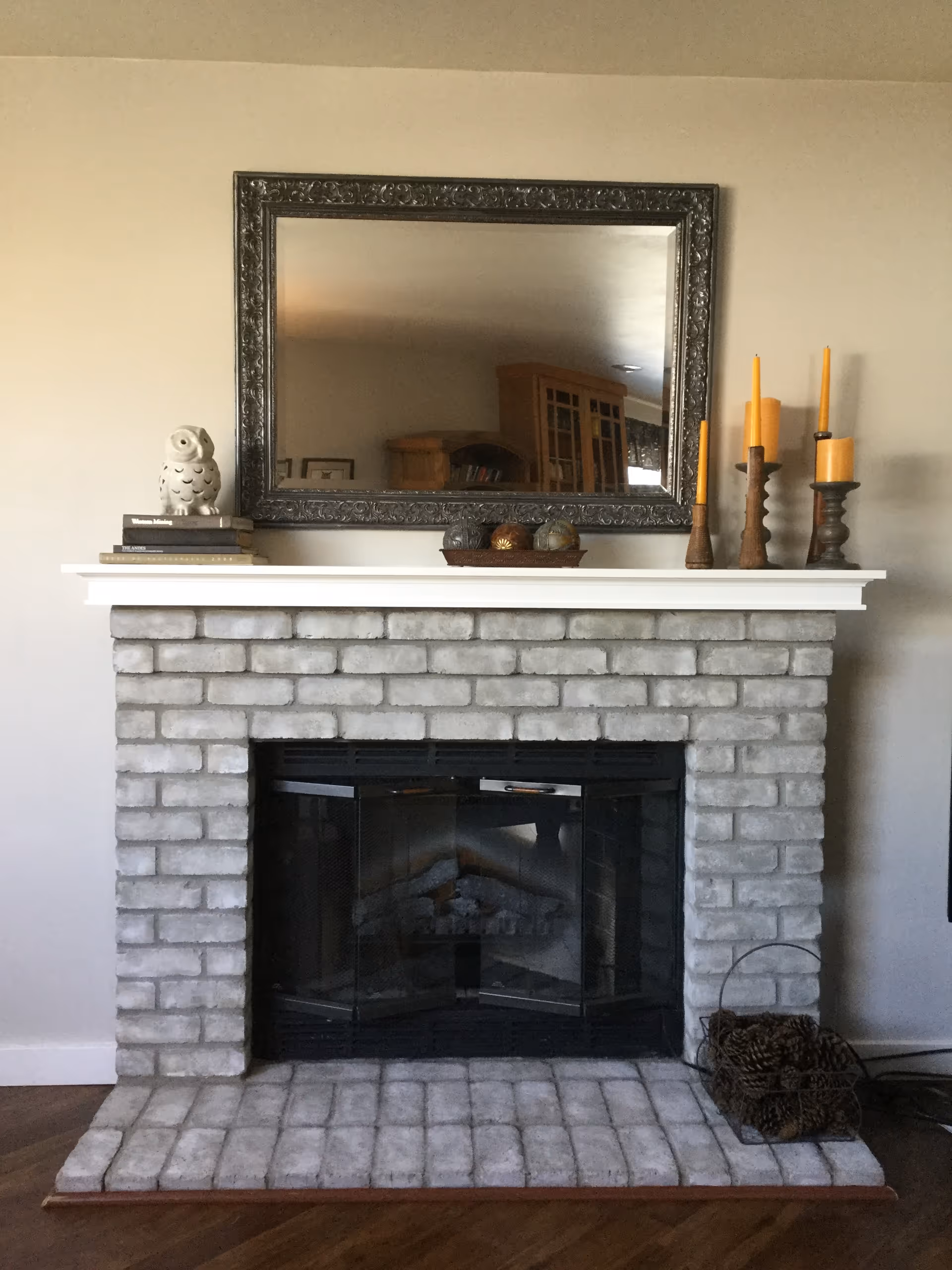 Brick fireplace with white mantel, ornate framed mirror, and decorative candleholders atop the mantle.