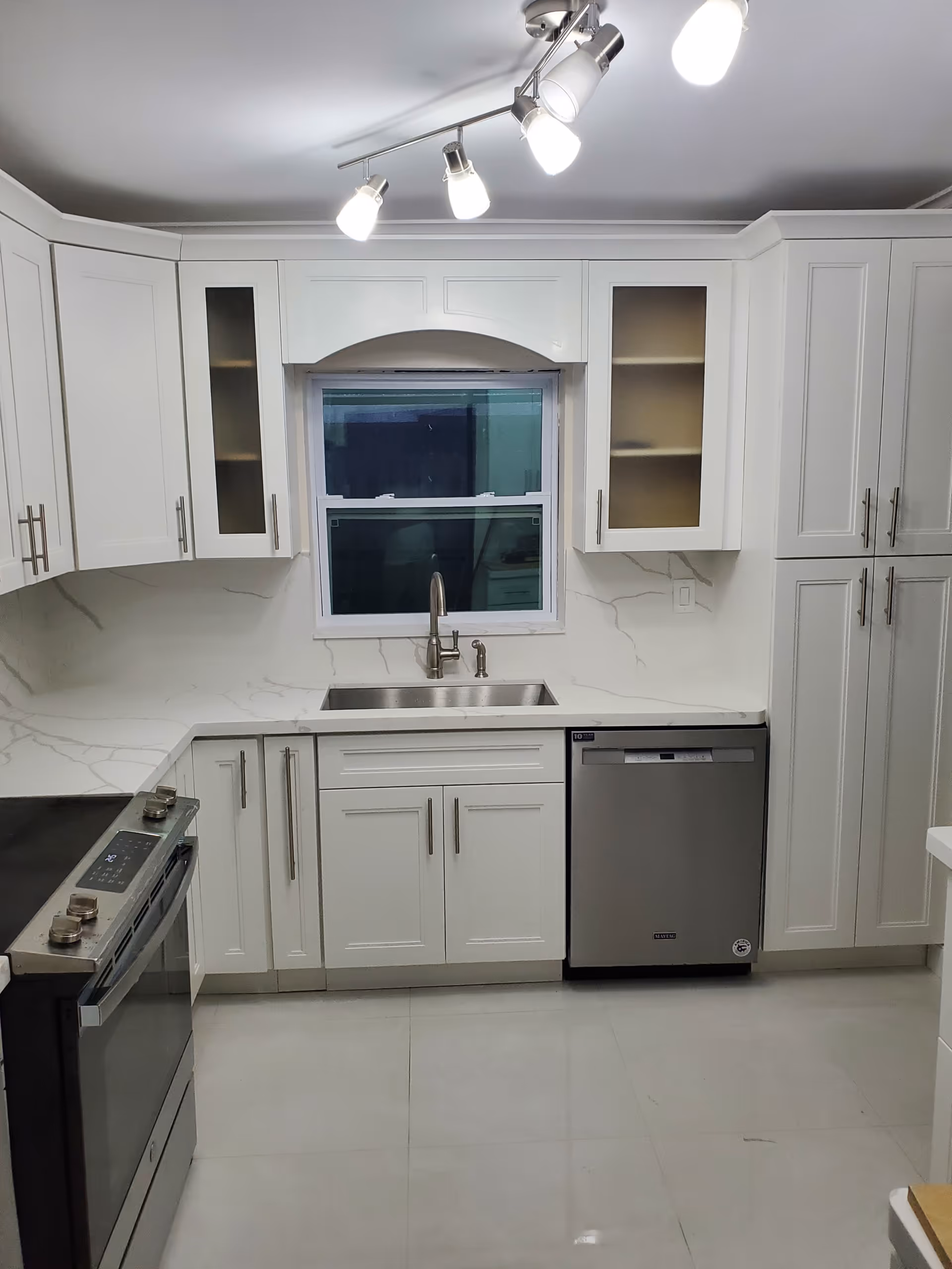 Bright white kitchen with cabinets, sink, dishwasher, and stainless appliances.