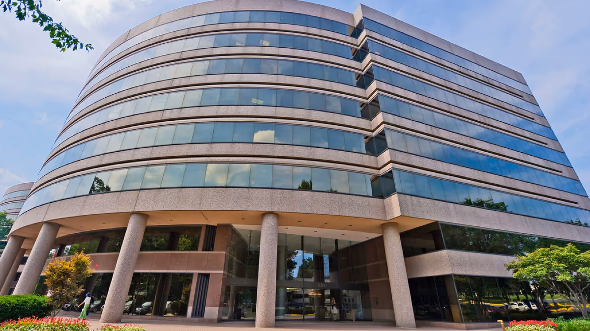 Modern glass-front senior living building with curved façade and tall entrance columns.