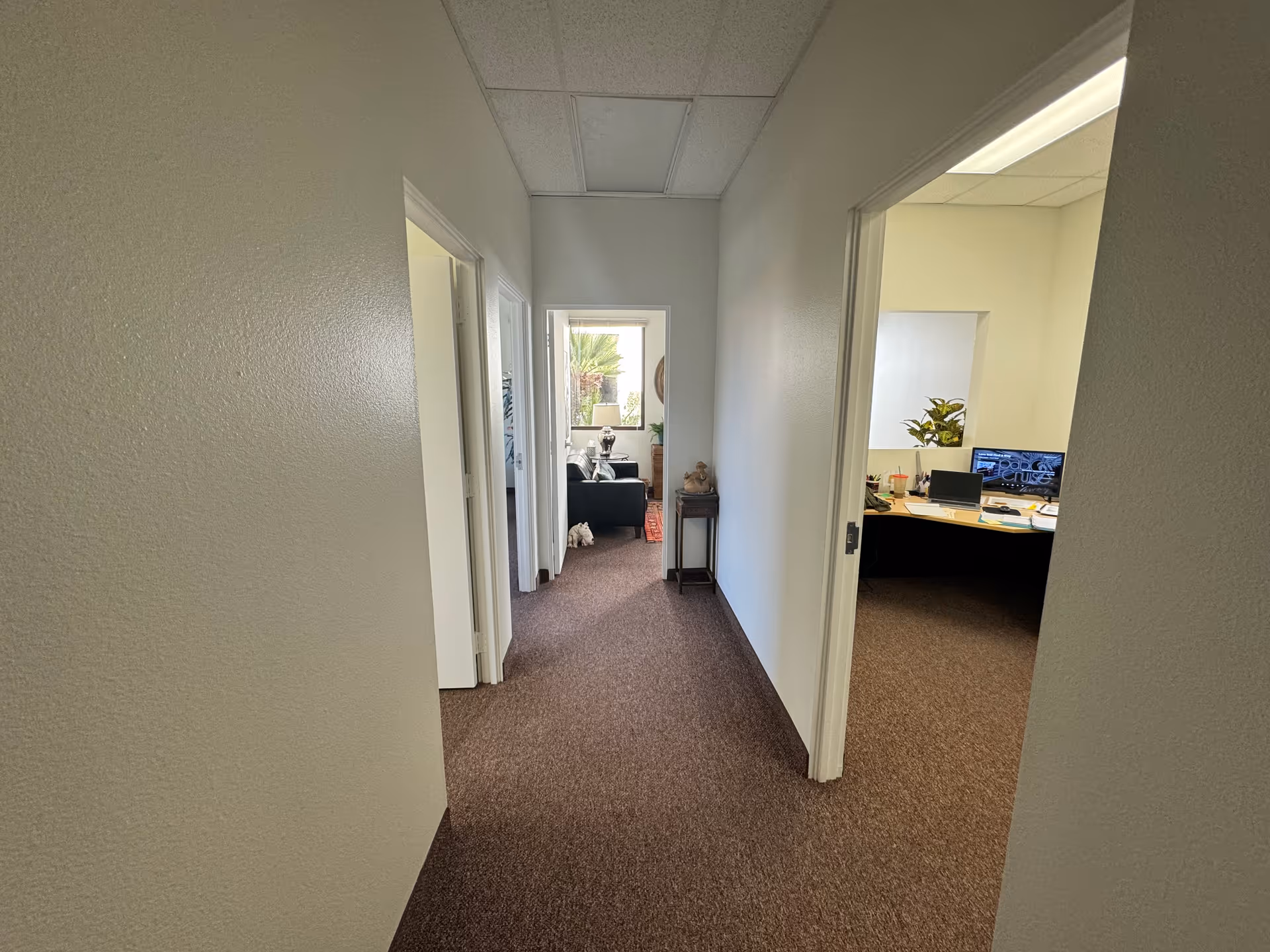 Long carpeted hallway inside a senior living facility, with open doorways and a desk visible.